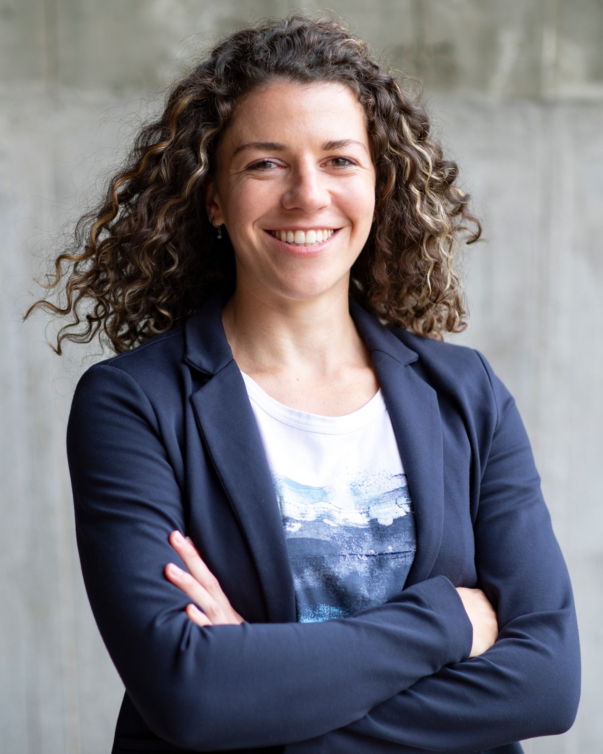 Een vrouw met krullend haar lacht met haar armen over elkaar