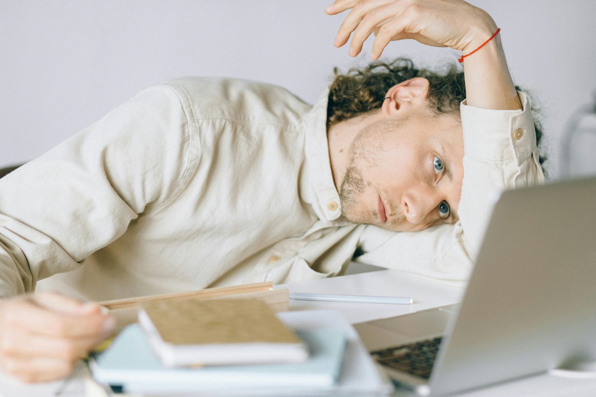 A man is laying on a desk with his head on a laptop computer.