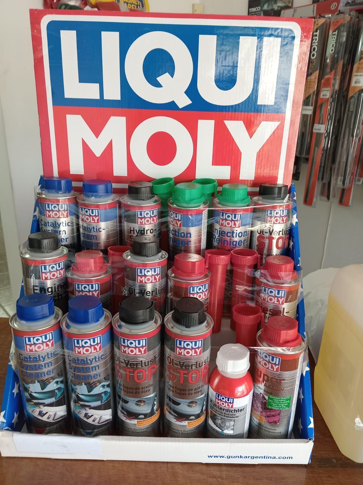 Exhibición de productos automotrices Liqui Moly en una tienda. Latas de aerosol de colores y una botella roja y blanca.