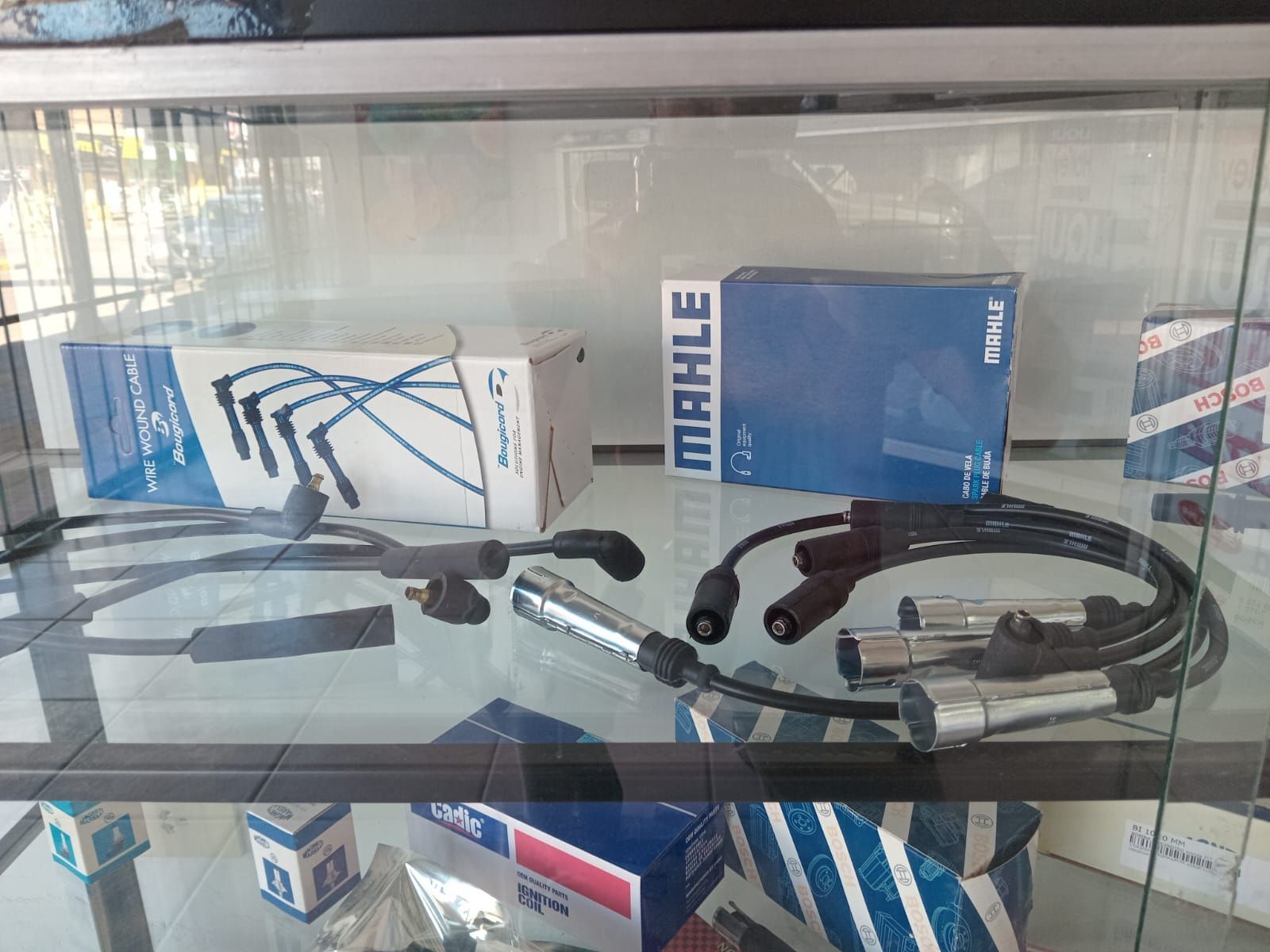 Bujías y cables expuestos en vitrina de cristal, con las cajas de la marca MAHLE.
