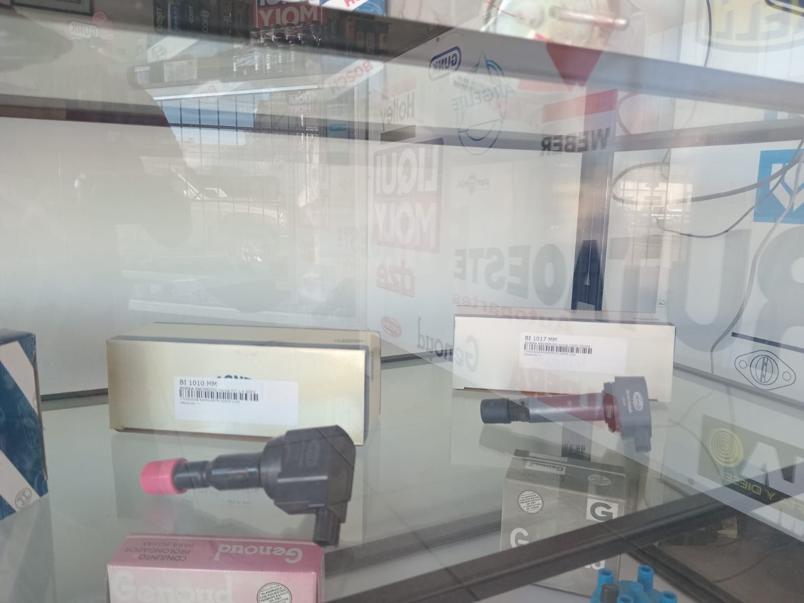 Vitrina con piezas de coche, cajas, bobinas de encendido y una gorra rosa.