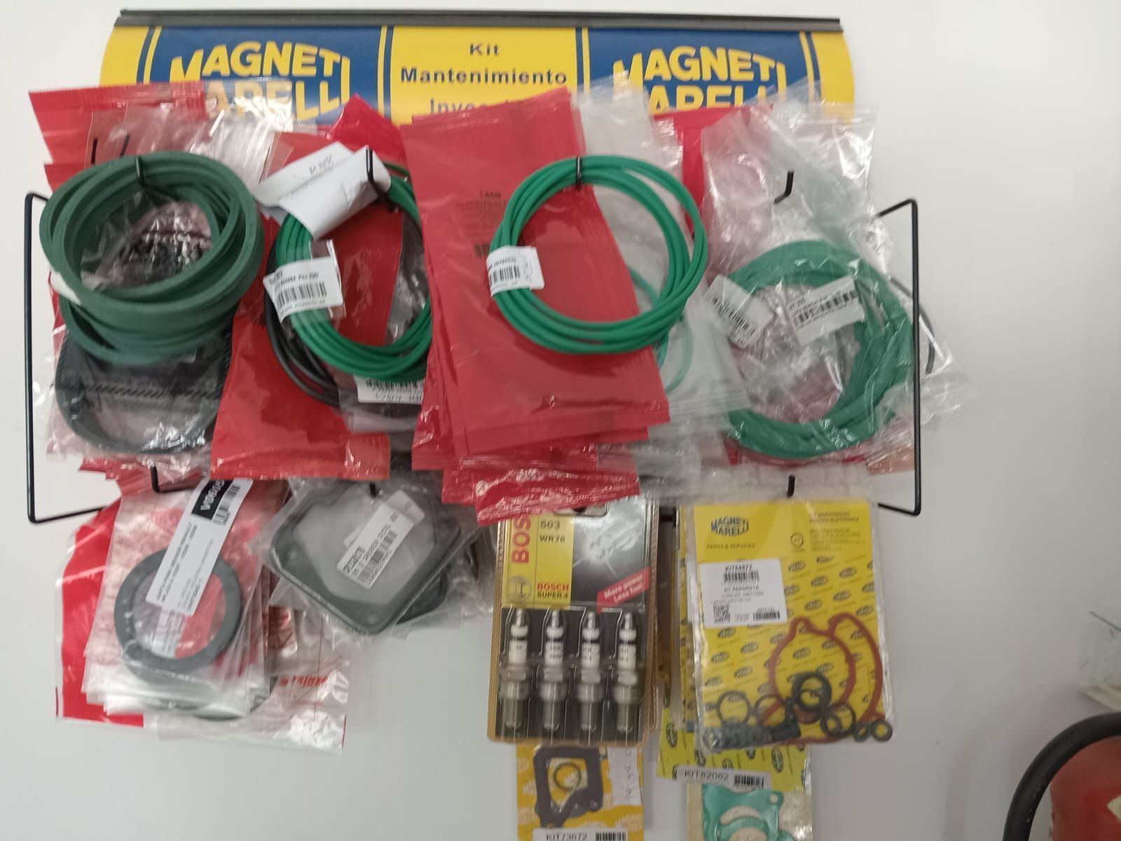 Exhibición de repuestos de automoción en bolsas: mangueras verdes, juntas, bujías y señalización Magneti Marelli.
