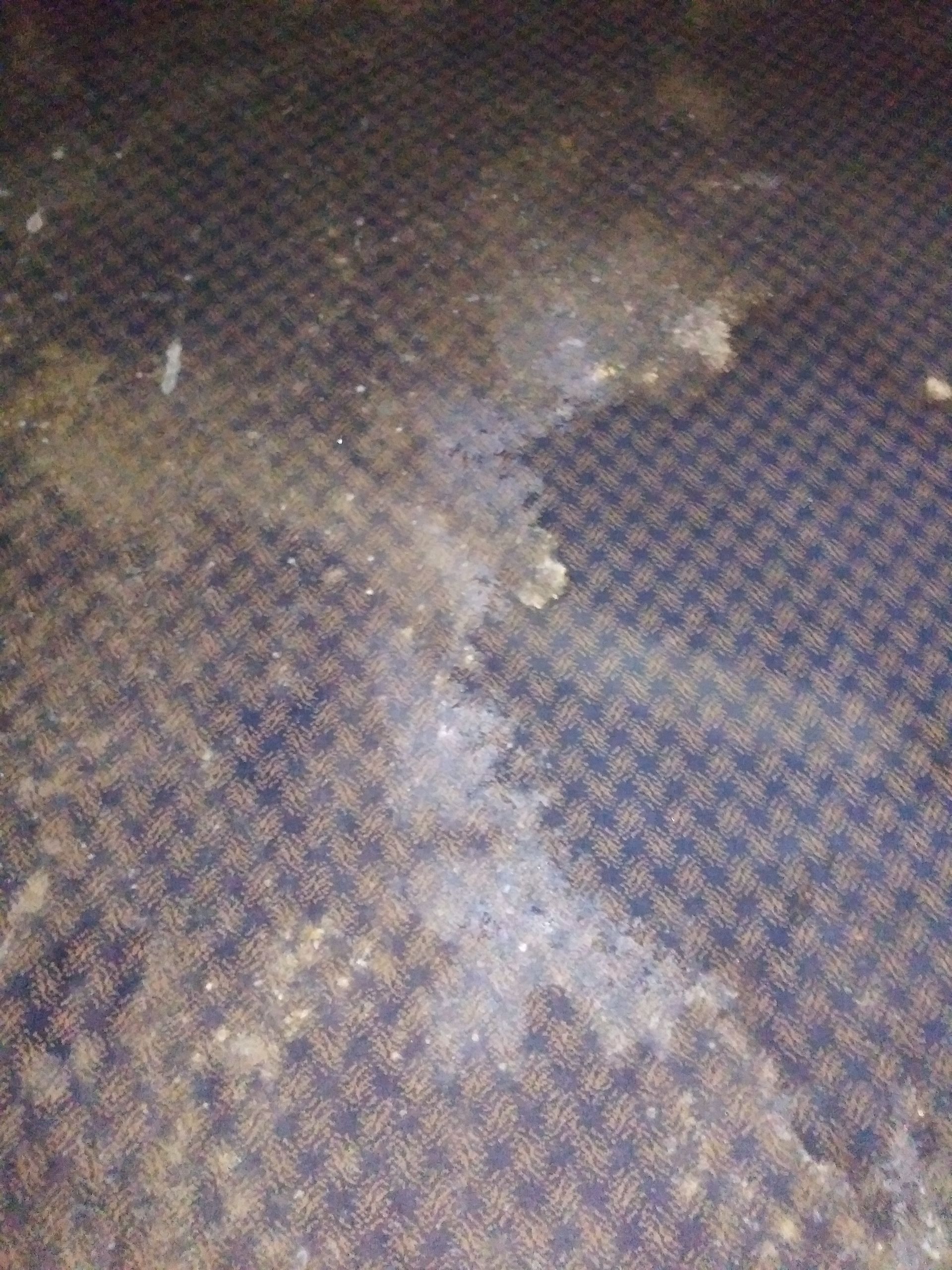 A close up of a dirty carpet with a stain on it.