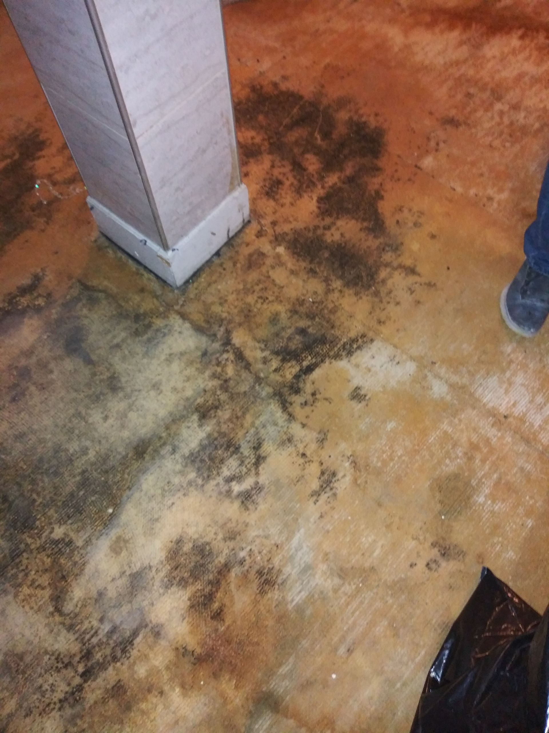 A person is standing on a dirty floor next to a pillar.