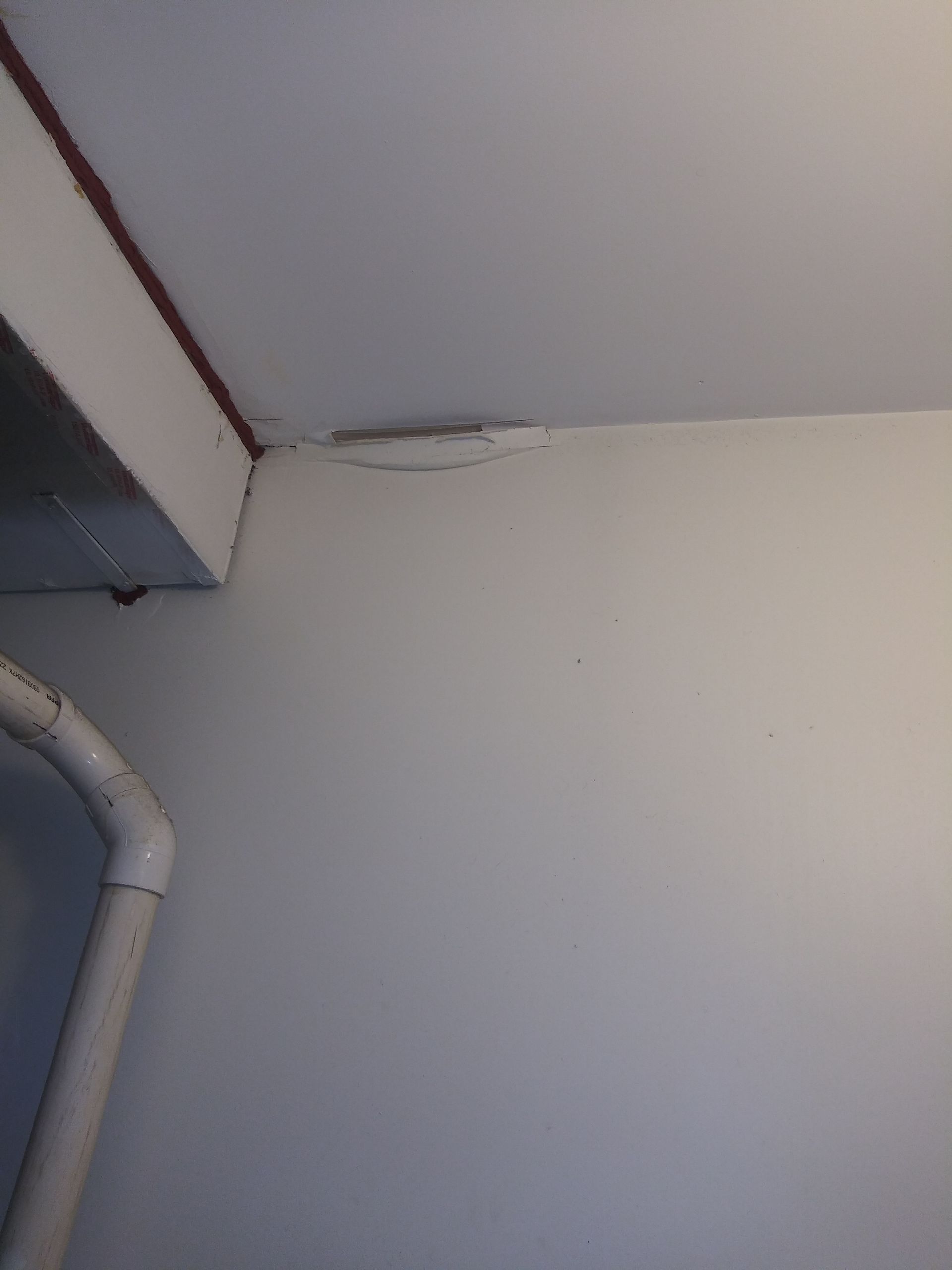 A white wall with a pipe coming out of it and a ceiling.