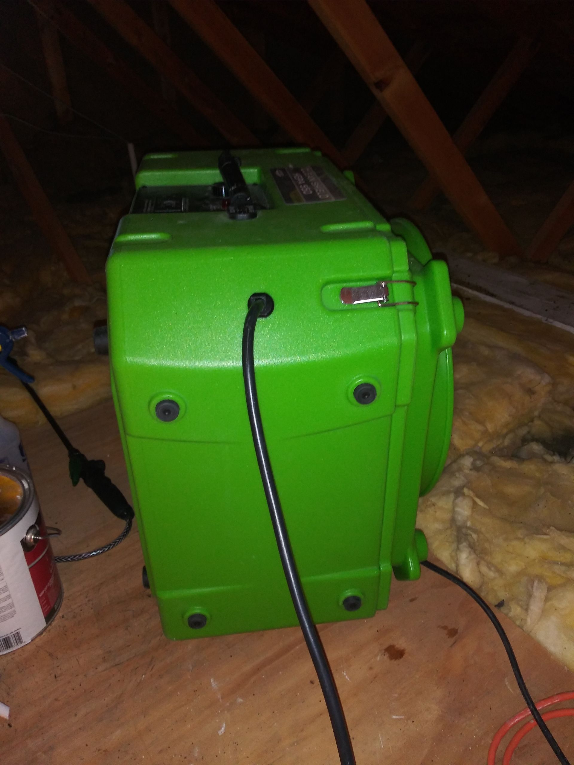 A green box with a cord attached to it is sitting on a wooden floor.