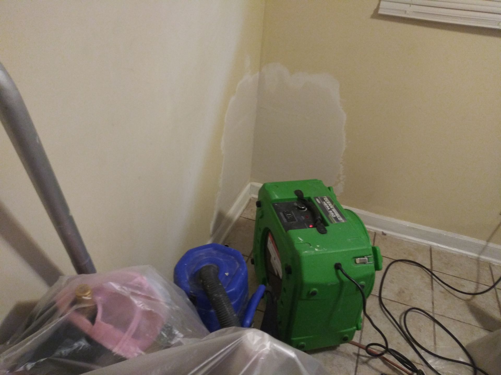 A green vacuum cleaner is sitting in a corner of a room.