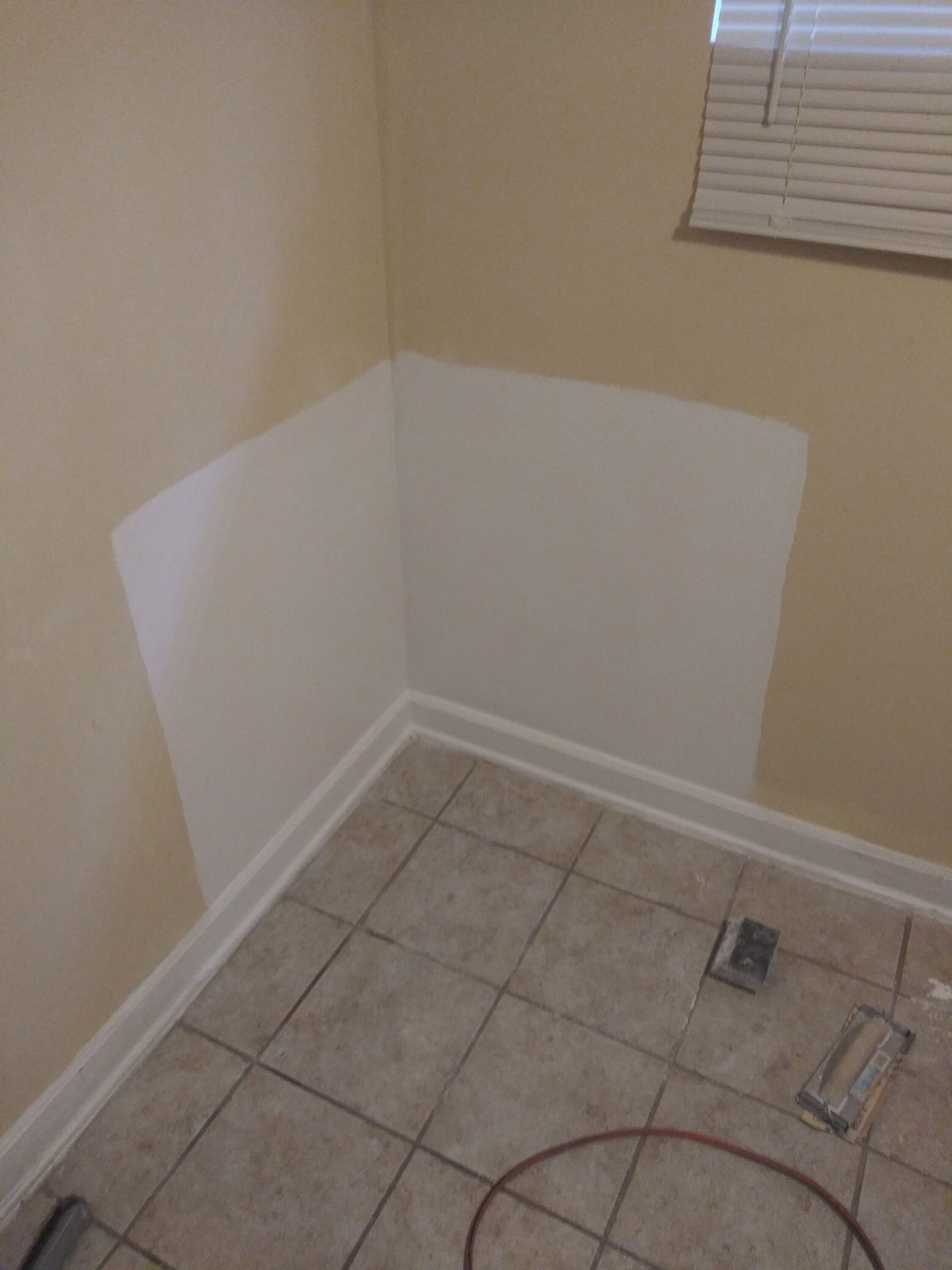A corner of a room with a window and tile floor