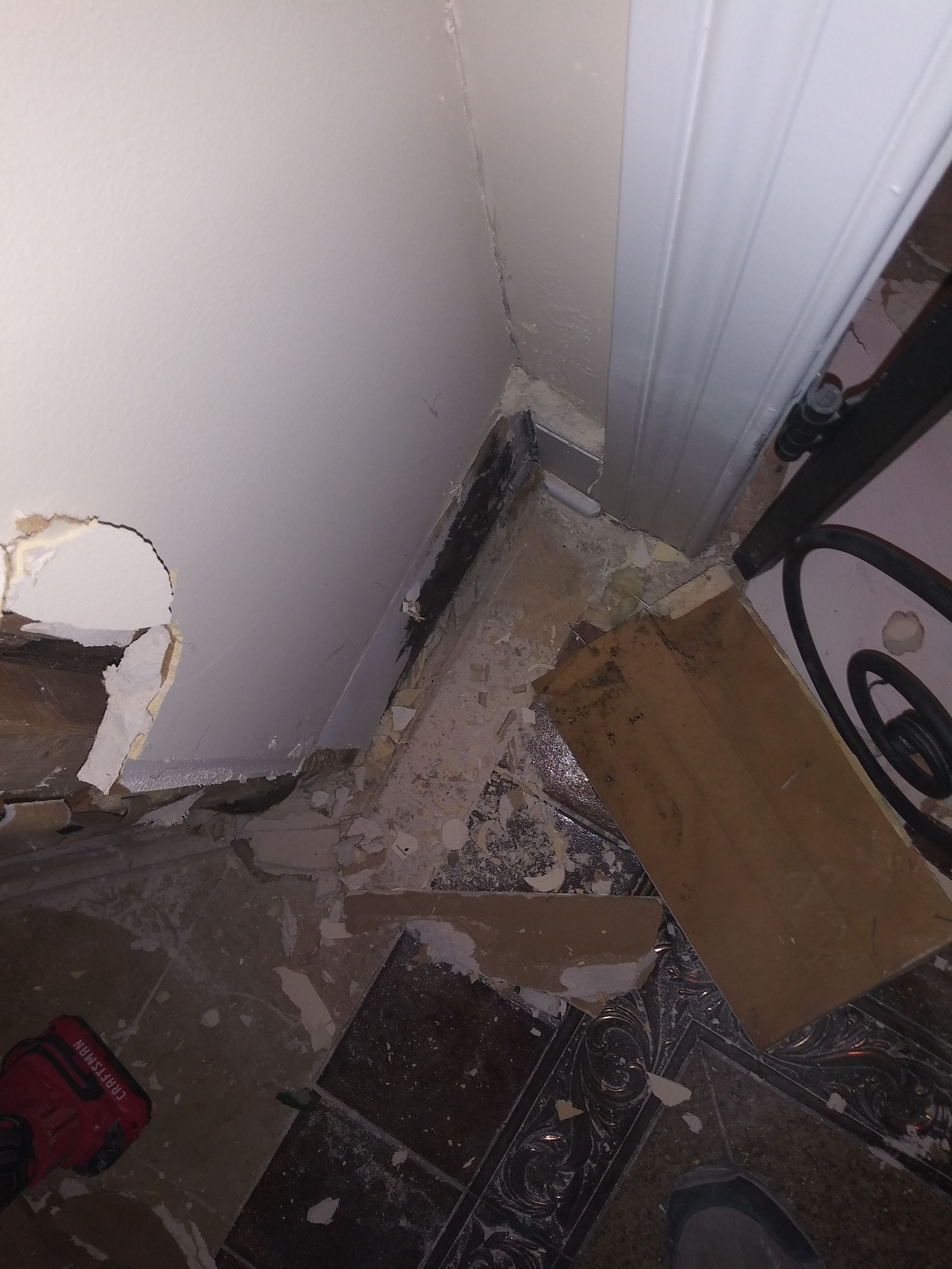 A room with a hole in the wall and a vacuum cleaner on the floor.