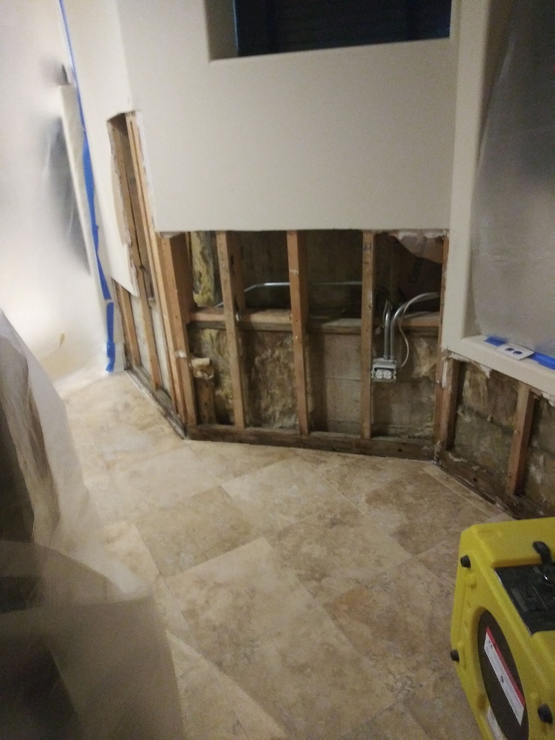 A room with a hole in the wall and a yellow box on the floor.