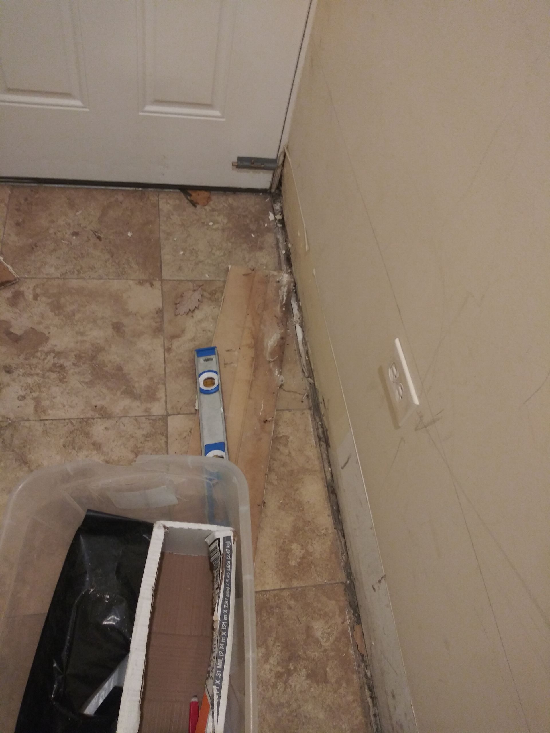 A box of tools sits on the floor next to a door and a level.