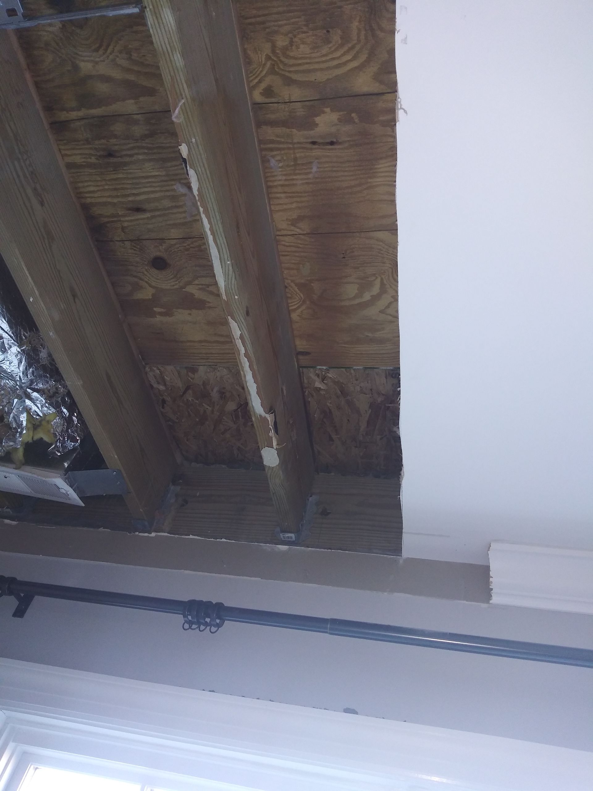 A ceiling with wooden beams and a white wall.