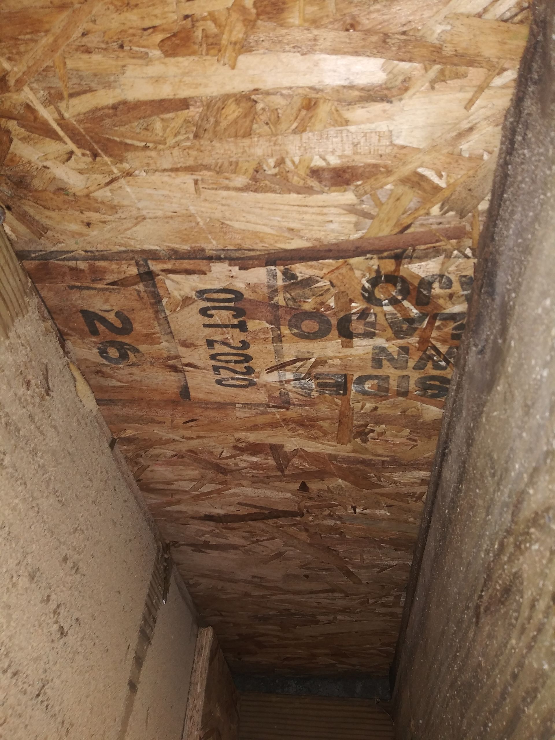 A narrow hallway with a wooden ceiling and a concrete wall.