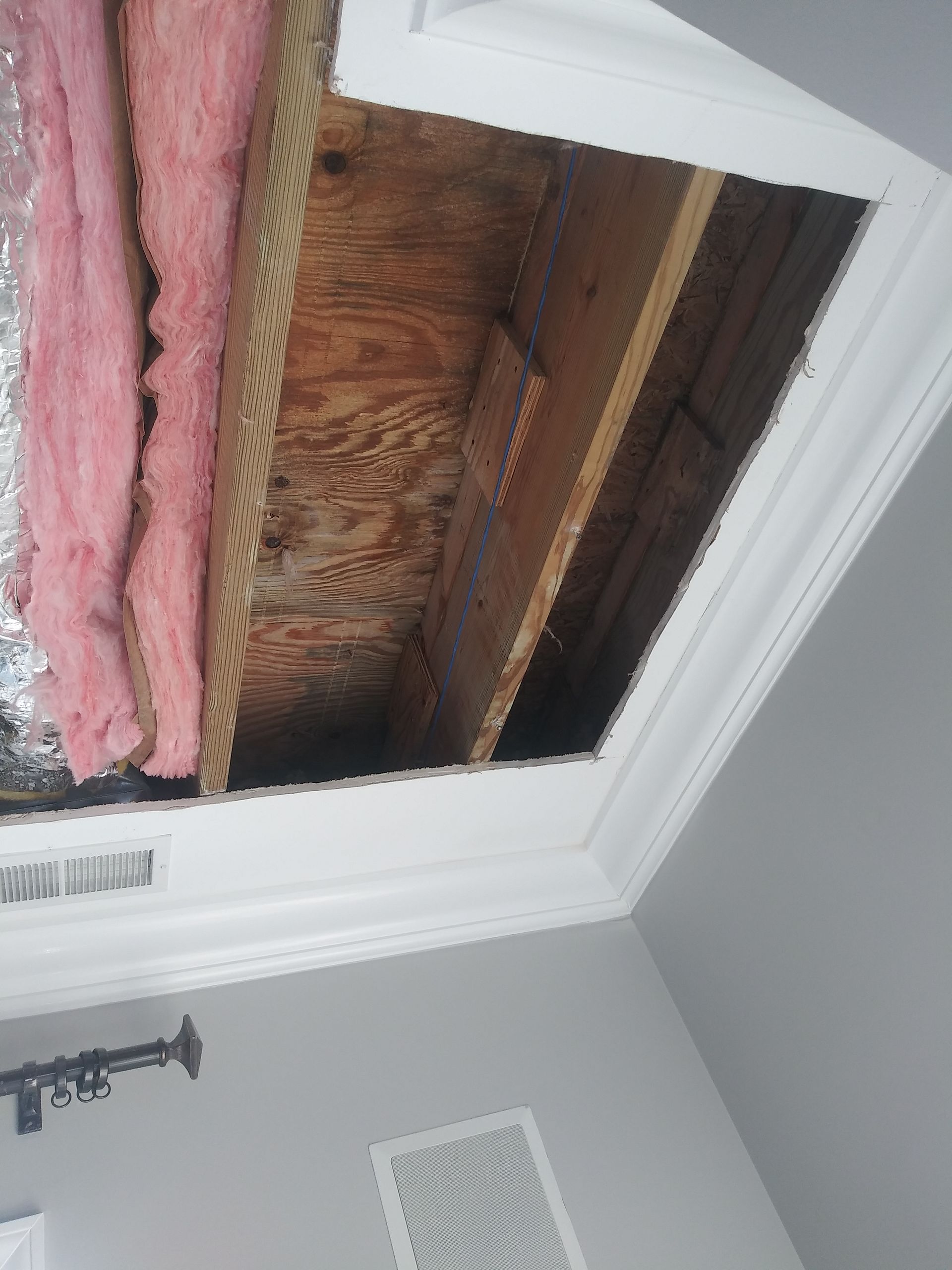 A room with a hole in the ceiling and pink insulation.