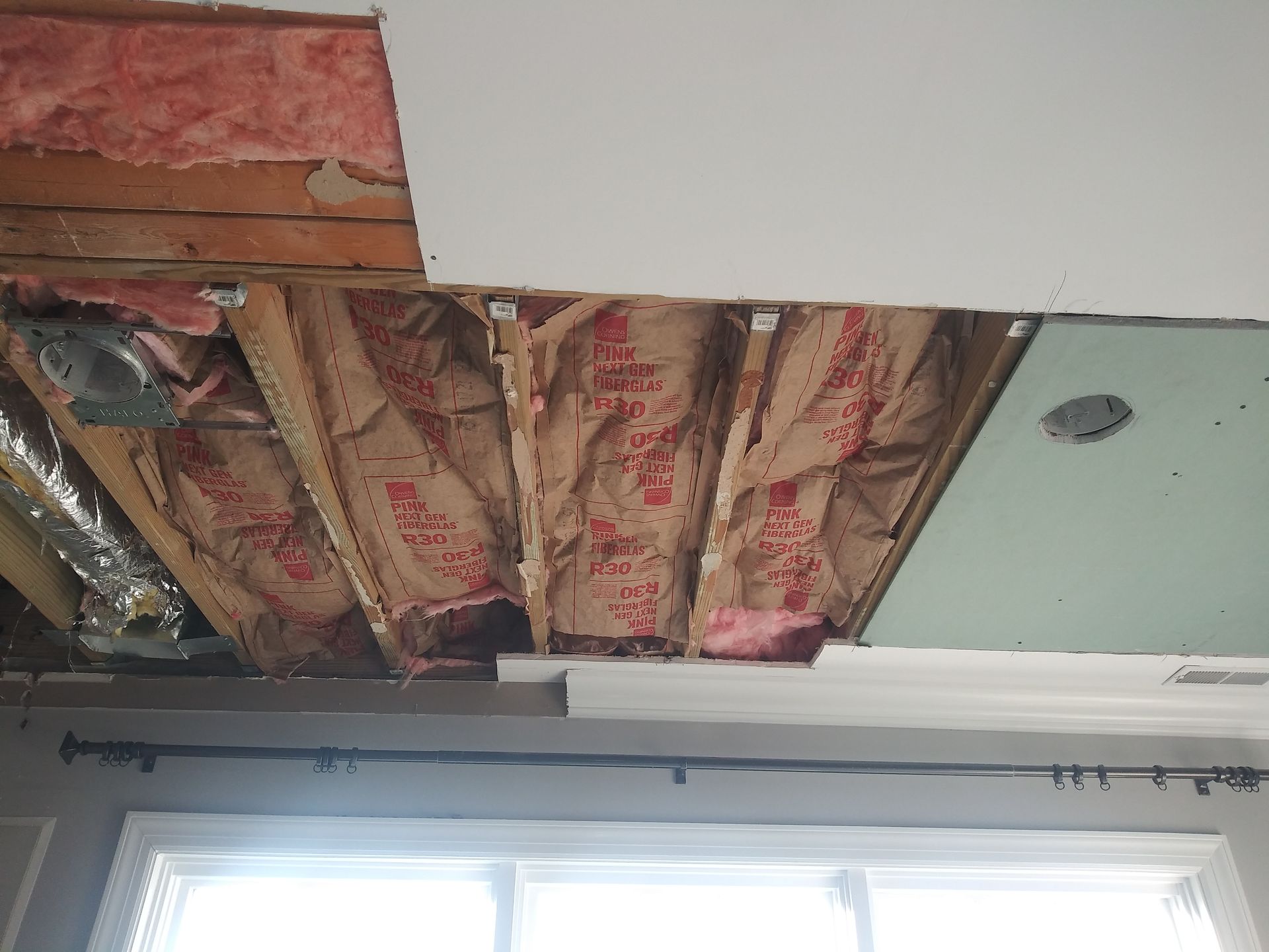 A room with a ceiling that is missing insulation and a window.