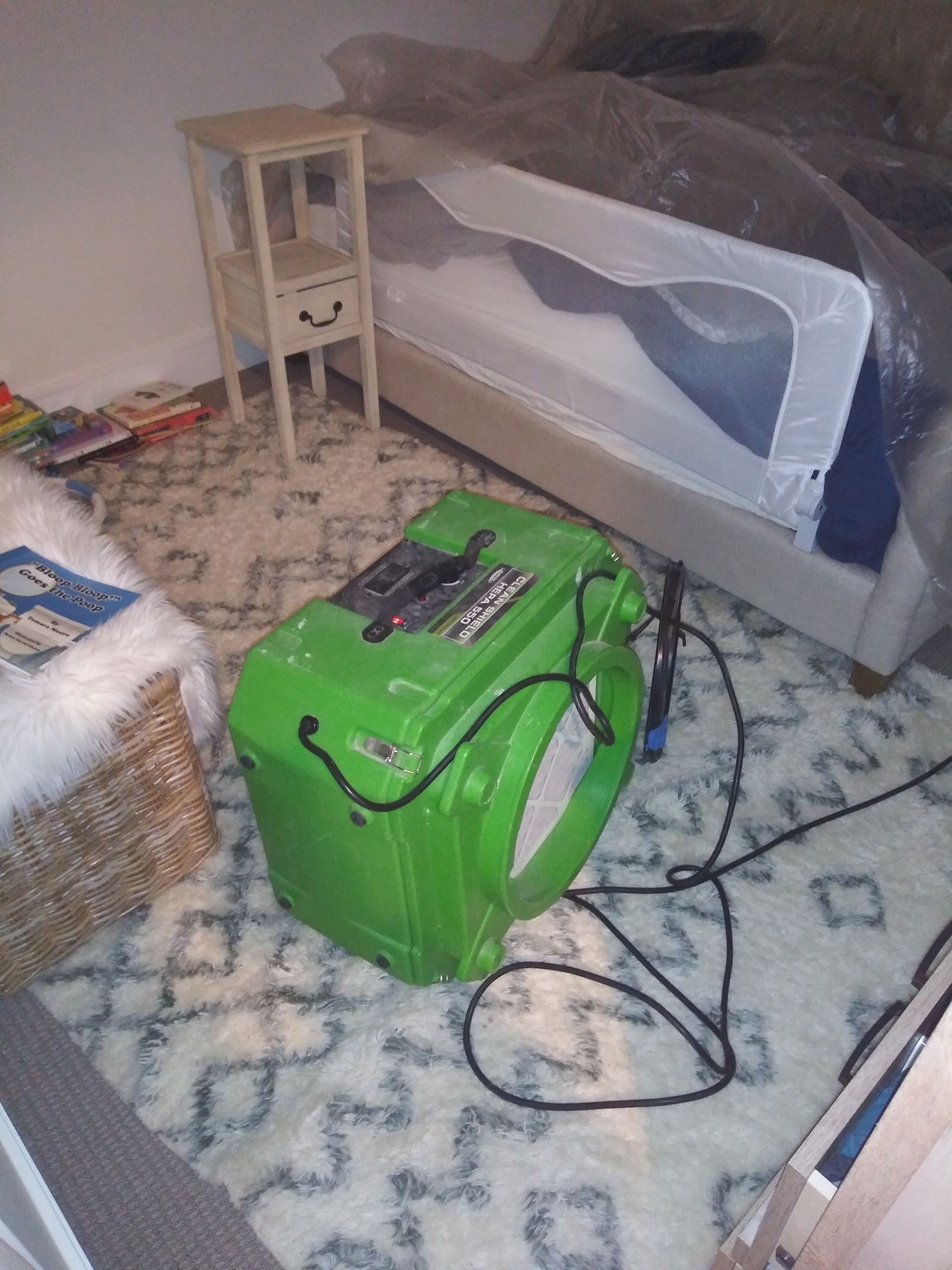 A green box is sitting on the floor in a room next to a bed.