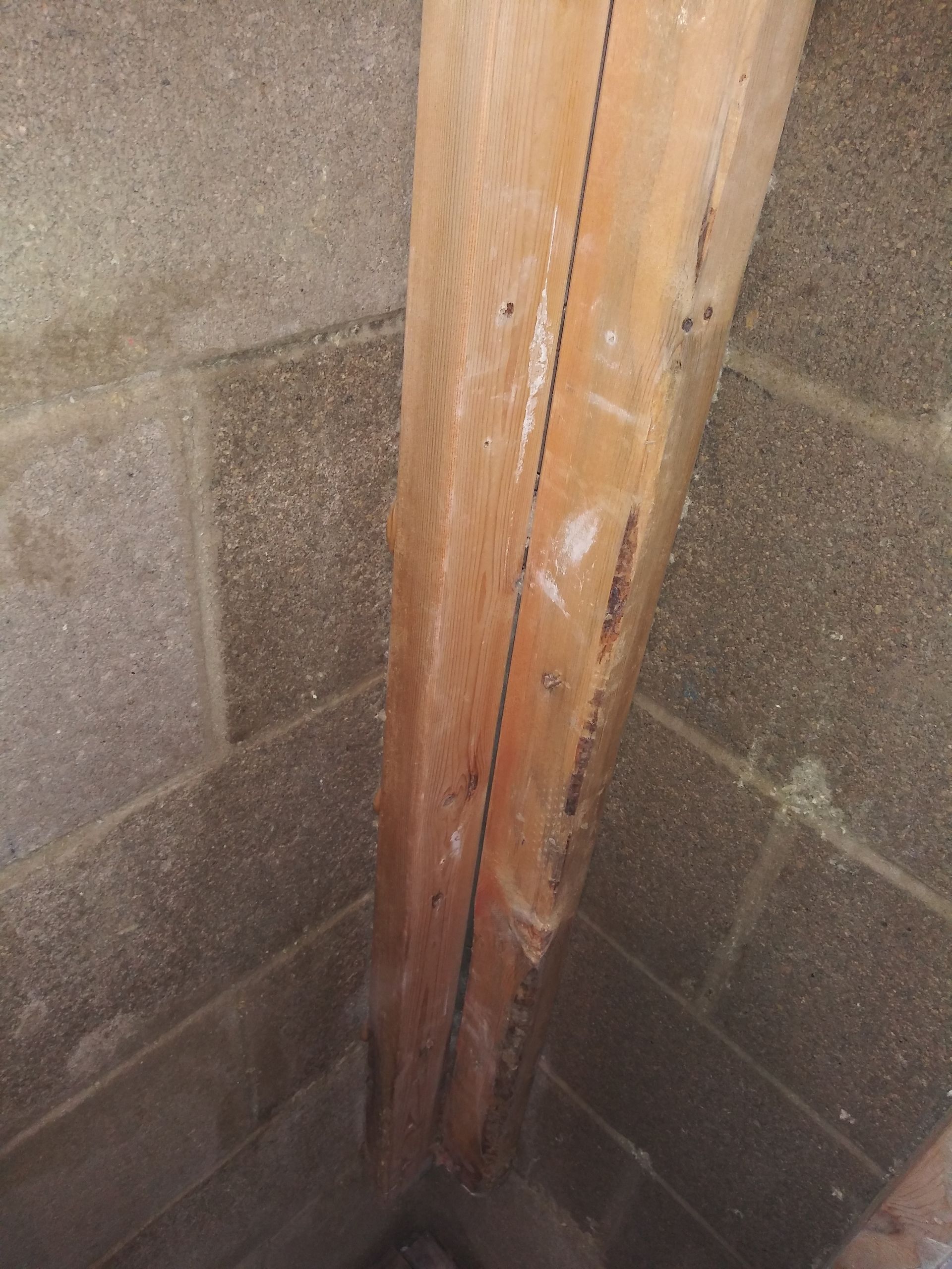 A wooden post is sitting in the corner of a brick wall.