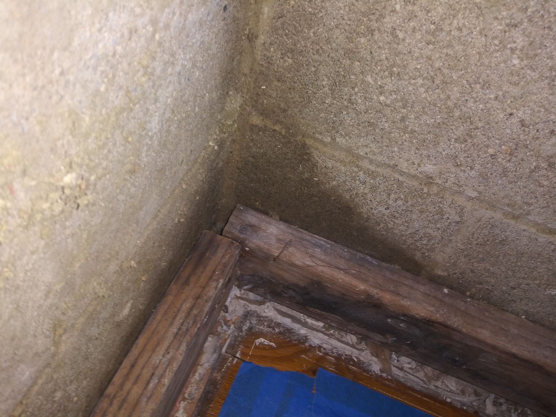 A corner of a room with a window frame and a concrete wall.