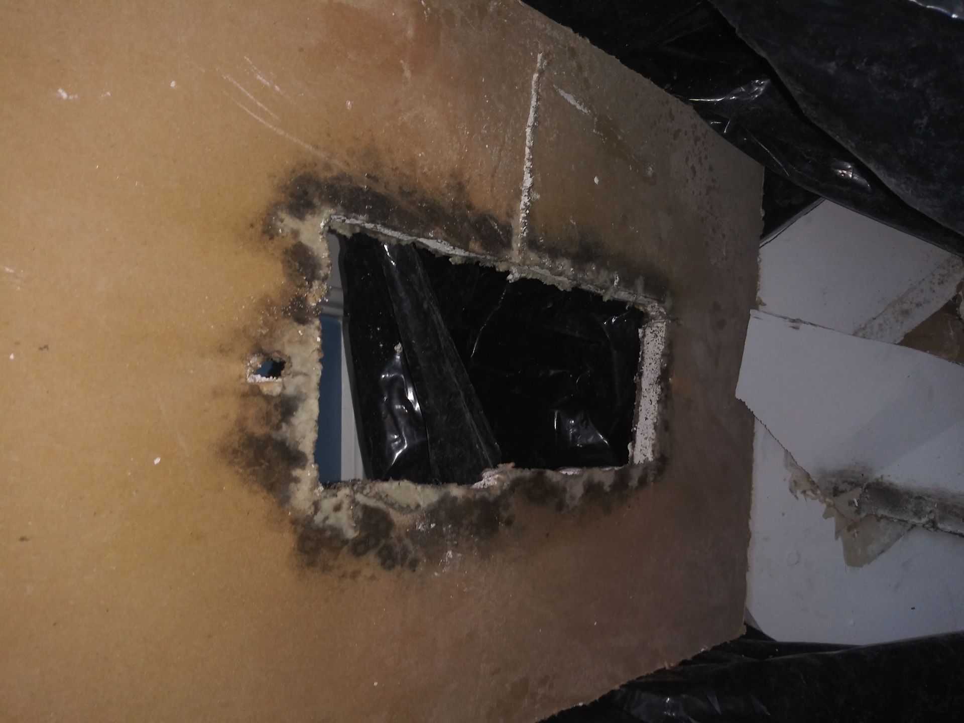 A hole in a wall with a black bag covering it