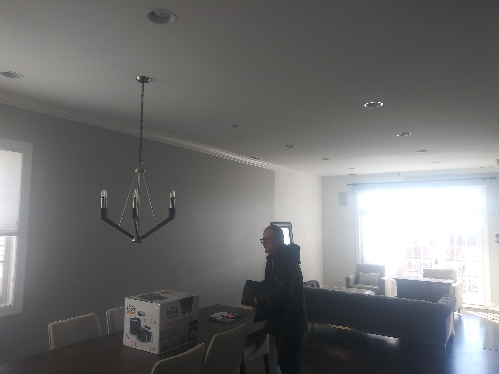 A man is standing in a living room with a chandelier hanging from the ceiling.