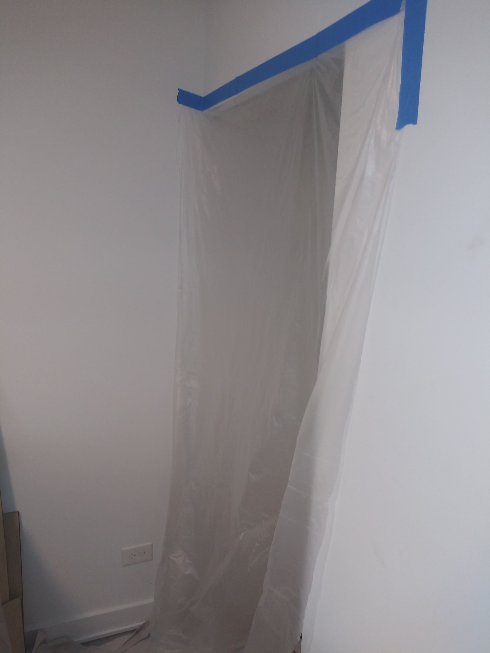 A room with a white curtain and blue tape on the wall.