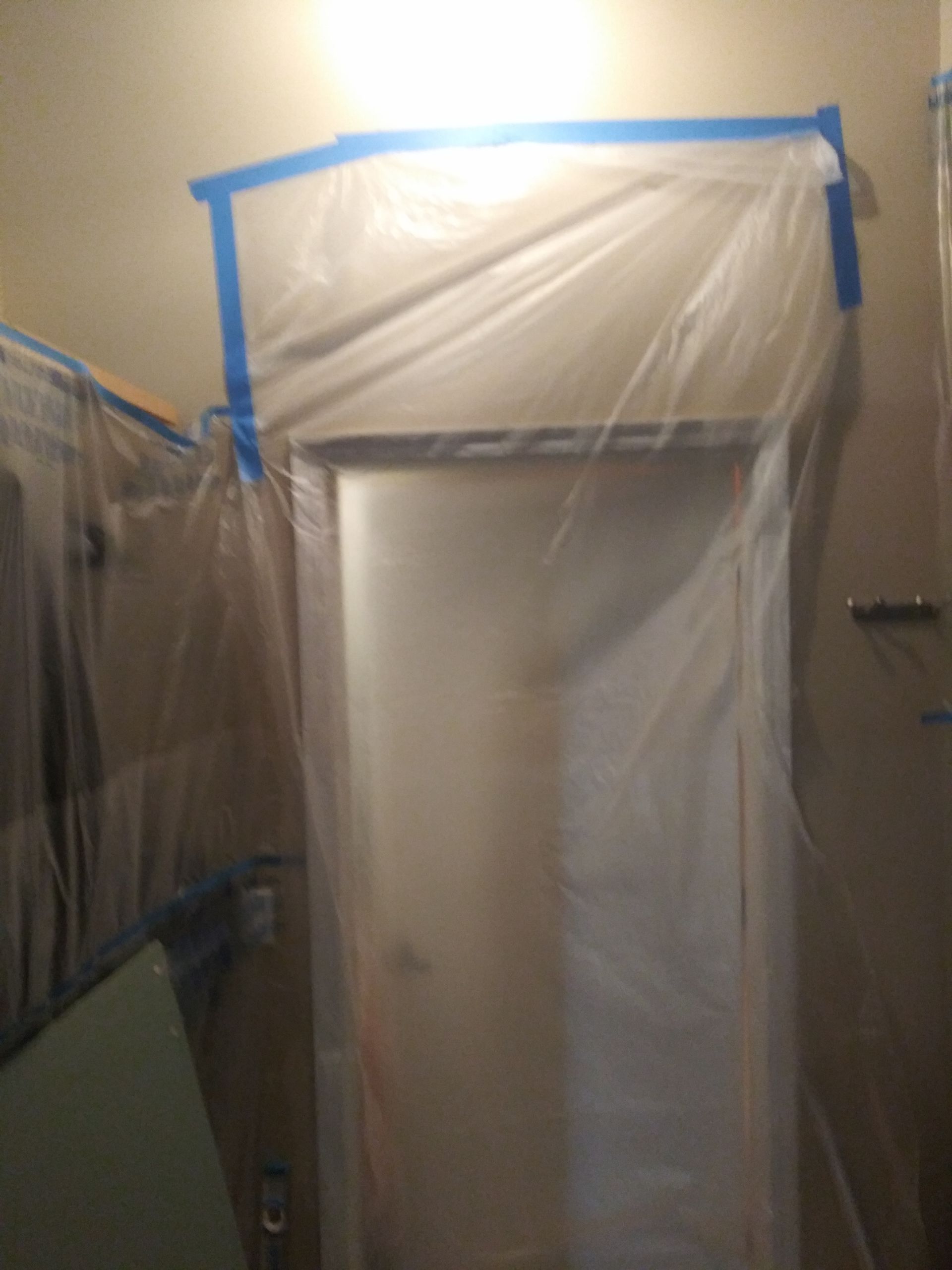 A door is covered in plastic and tape in a room.