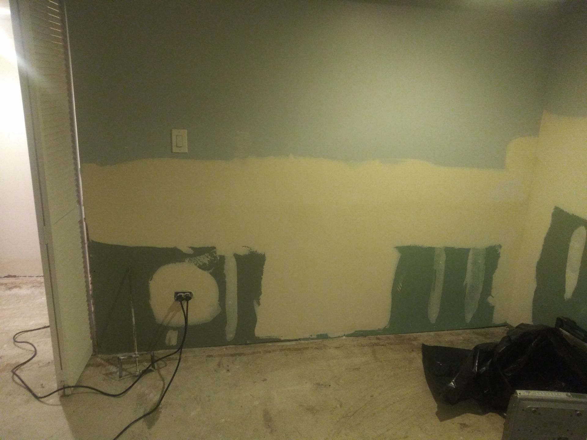 A room with a wall that is being painted and a laptop on the floor.