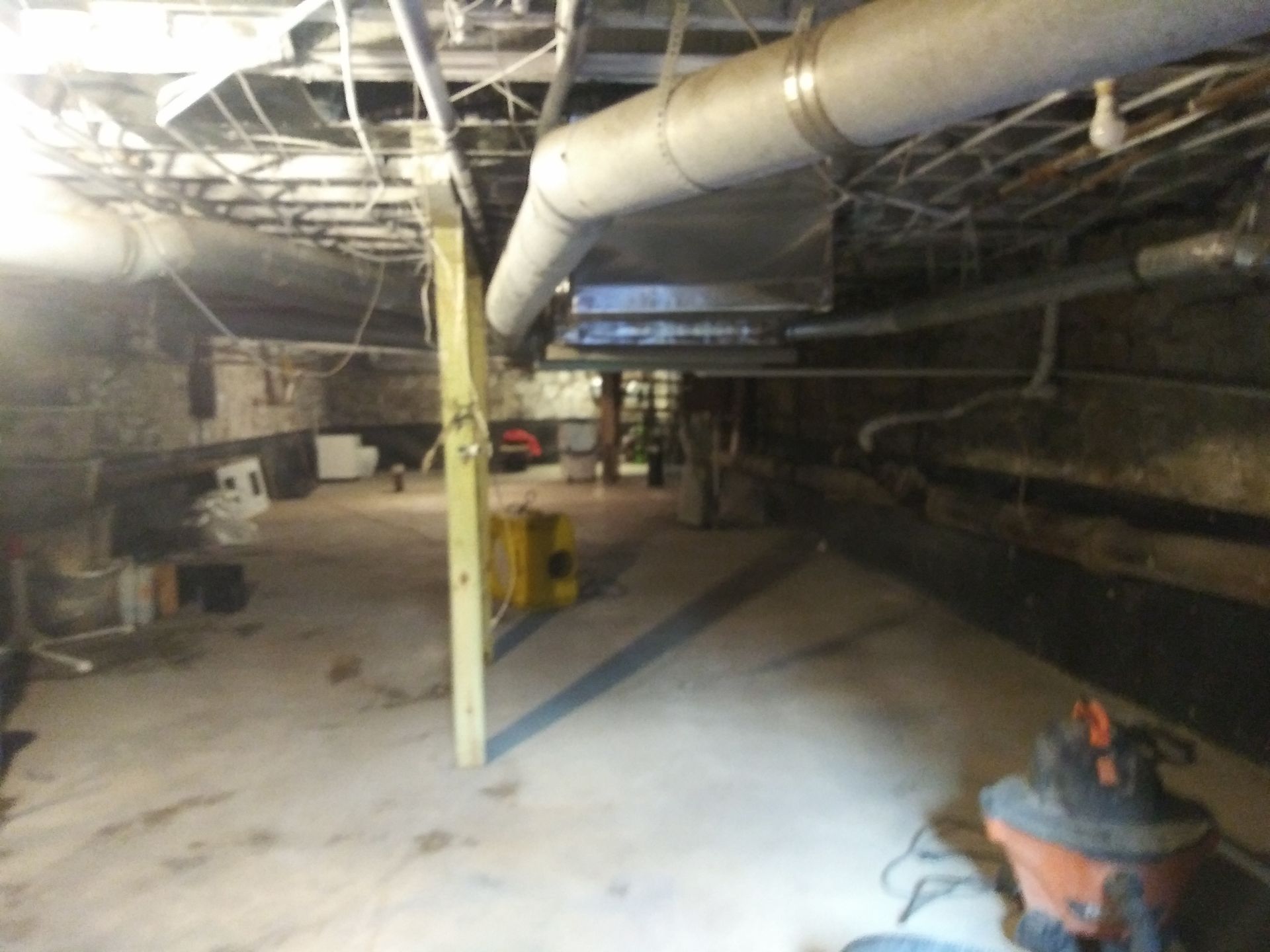 An empty basement with pipes and a vacuum cleaner