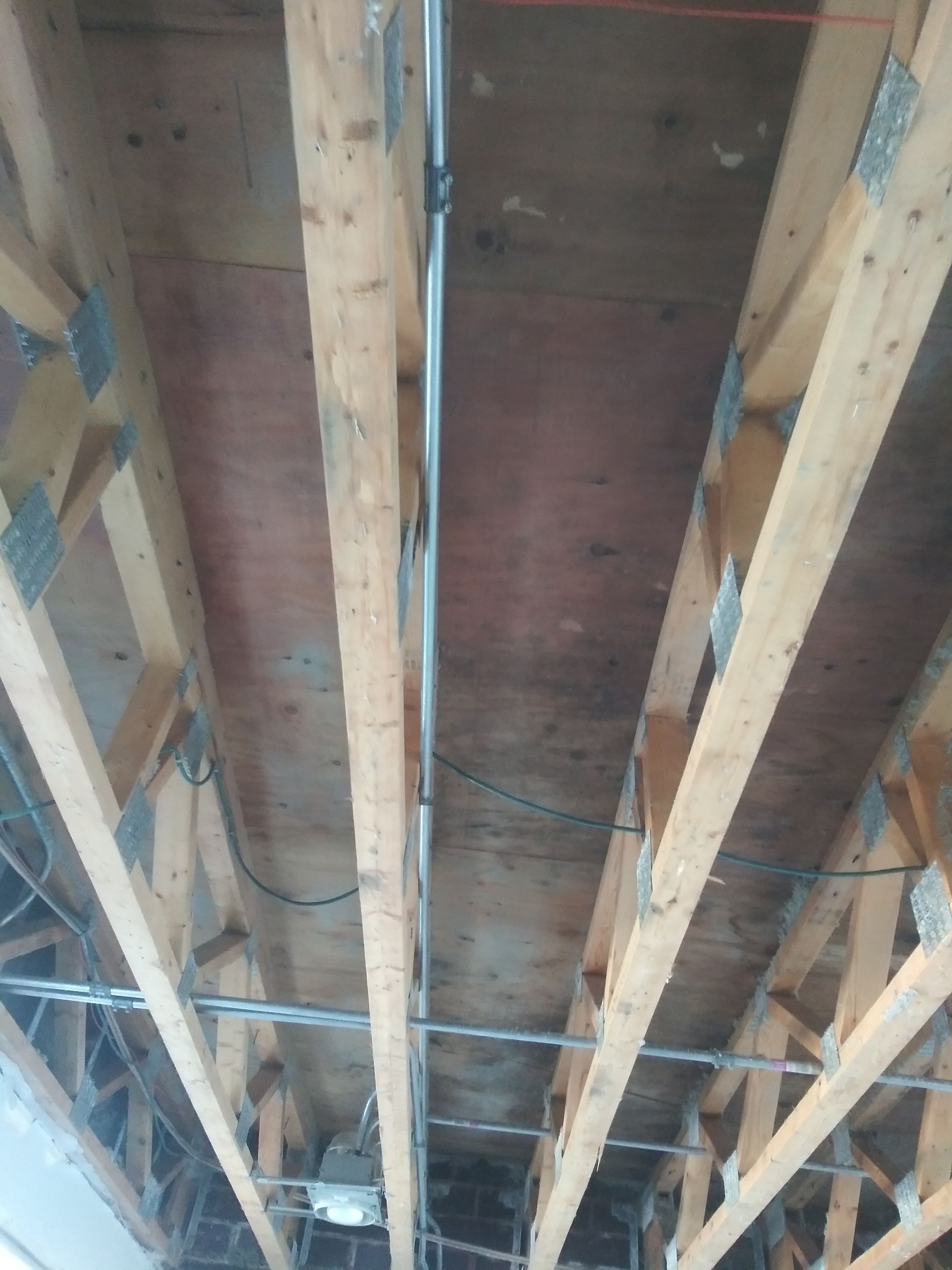 The ceiling of a building with wooden beams and wires.