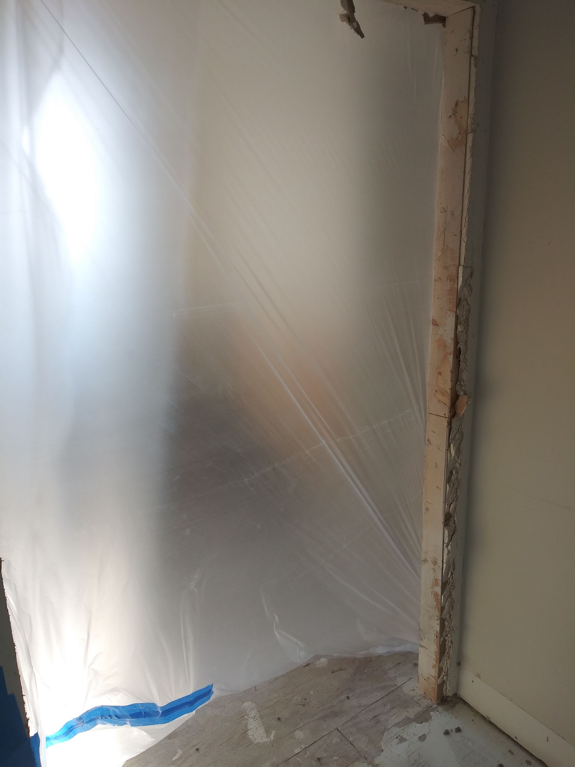 A room with a plastic sheet on the wall and a door.