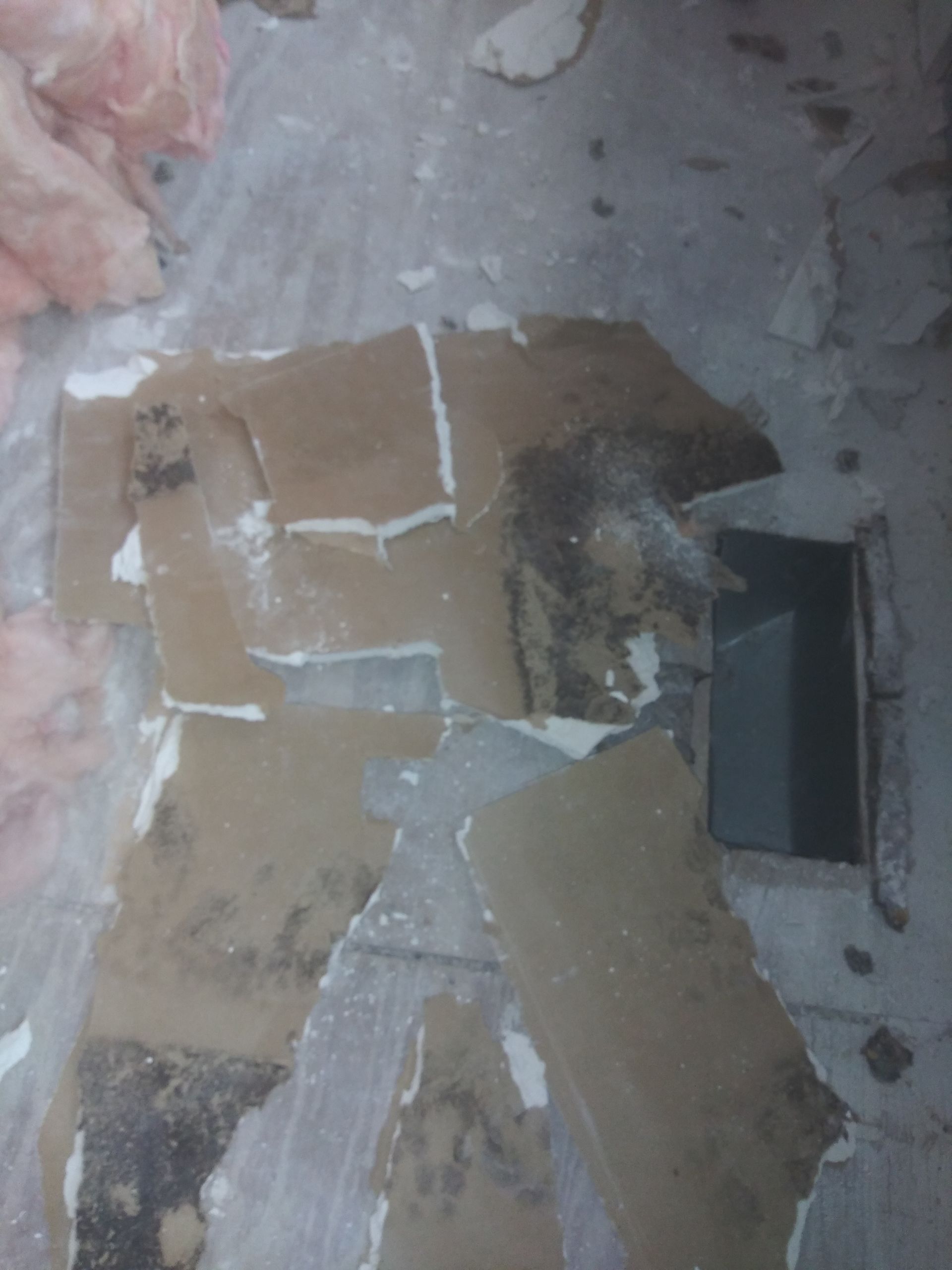 A piece of cardboard is laying on the floor next to a hole in the wall.