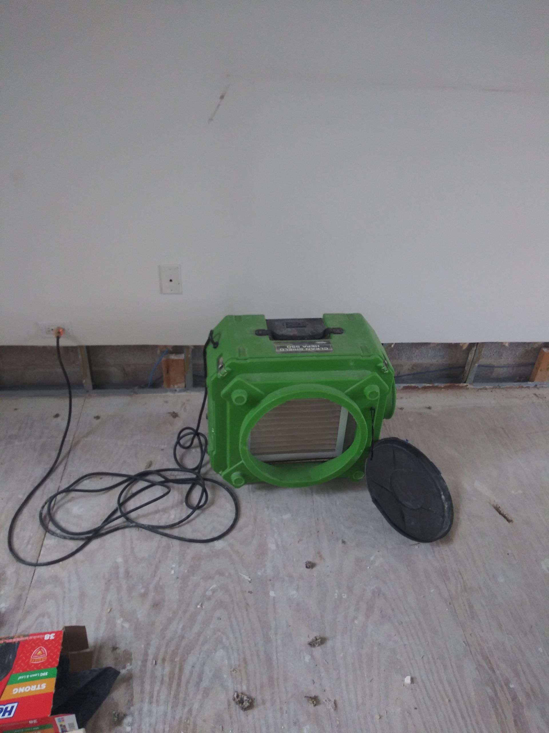 A green box is sitting on a wooden floor next to a wall.
