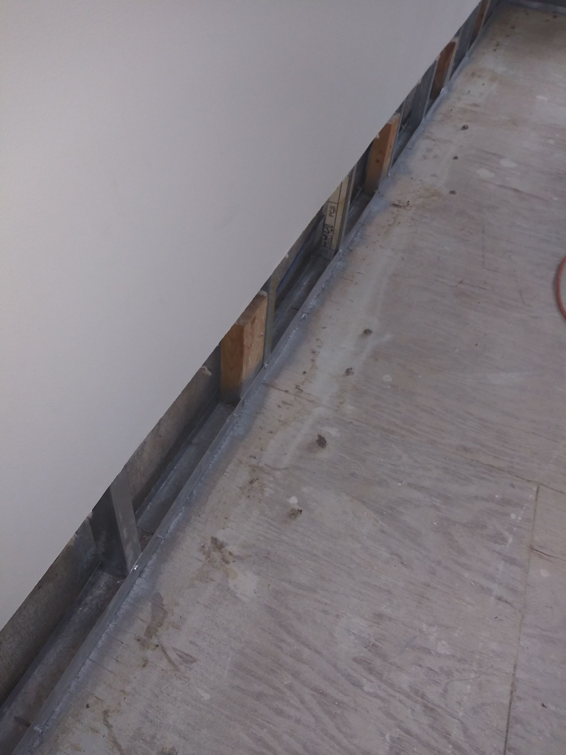 A corner of a room with a white wall and a wooden floor.