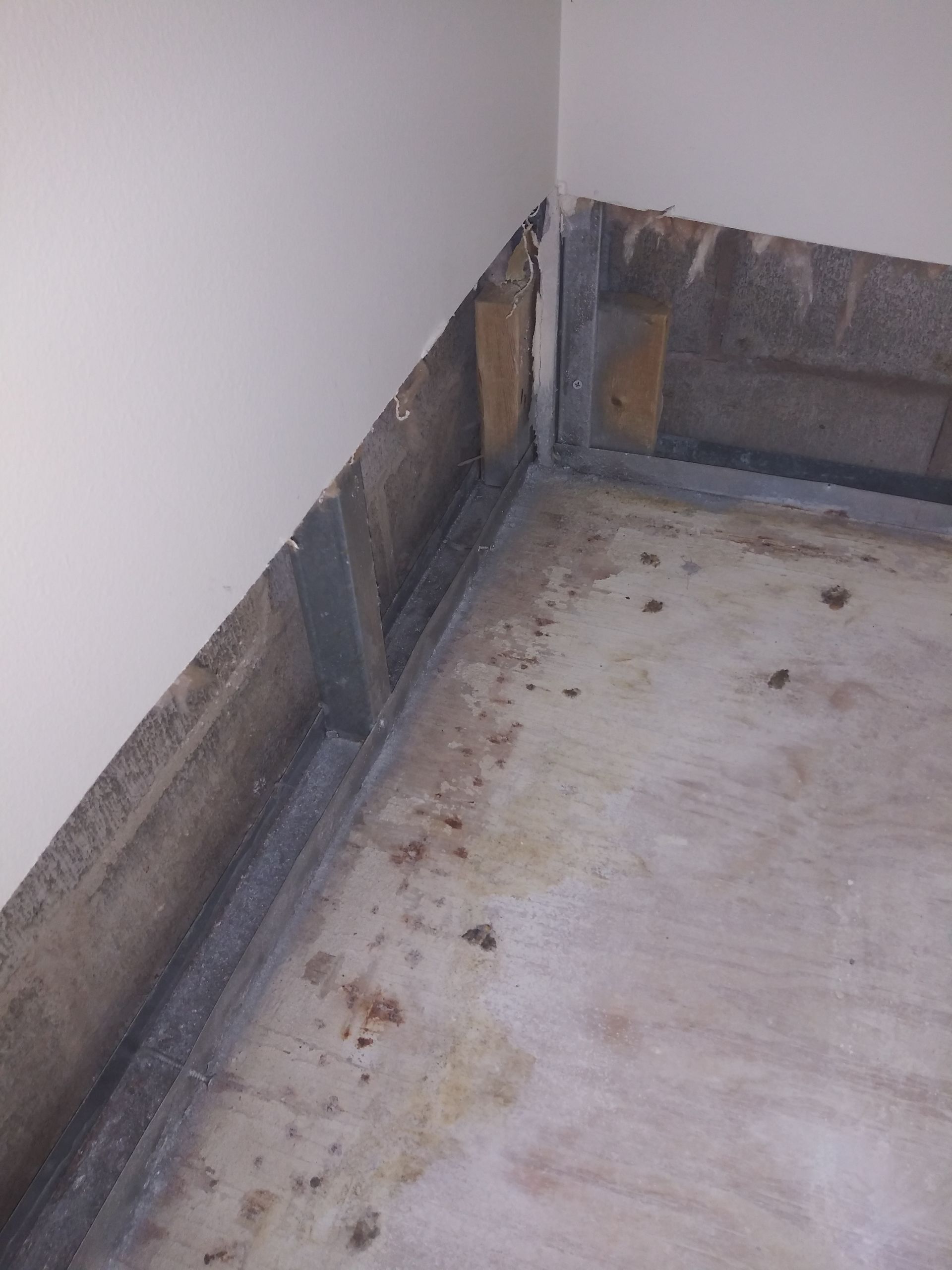 A corner of a room with a dirty floor and a brick wall.