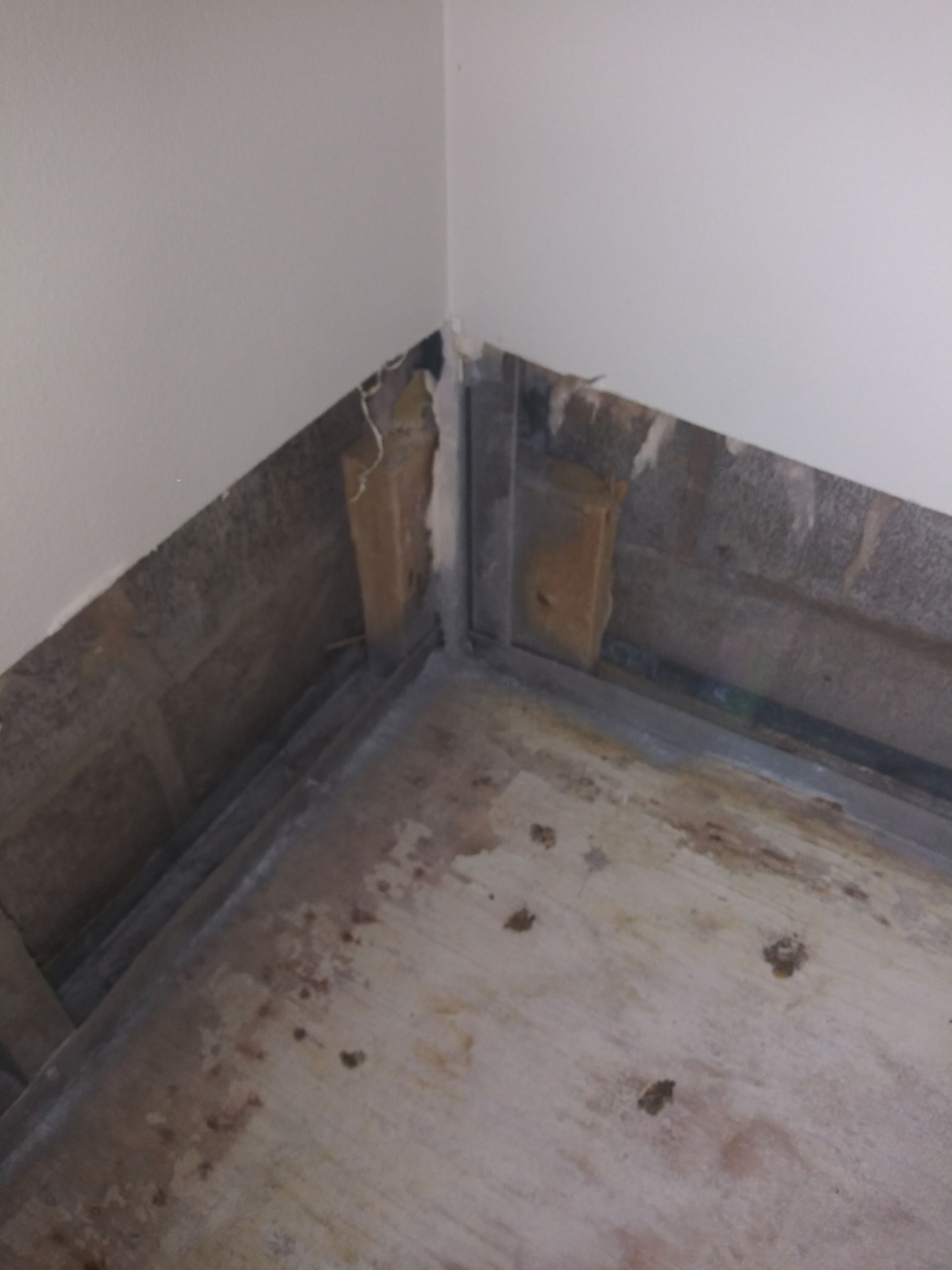 A corner of a room with a white wall and a dirty floor.