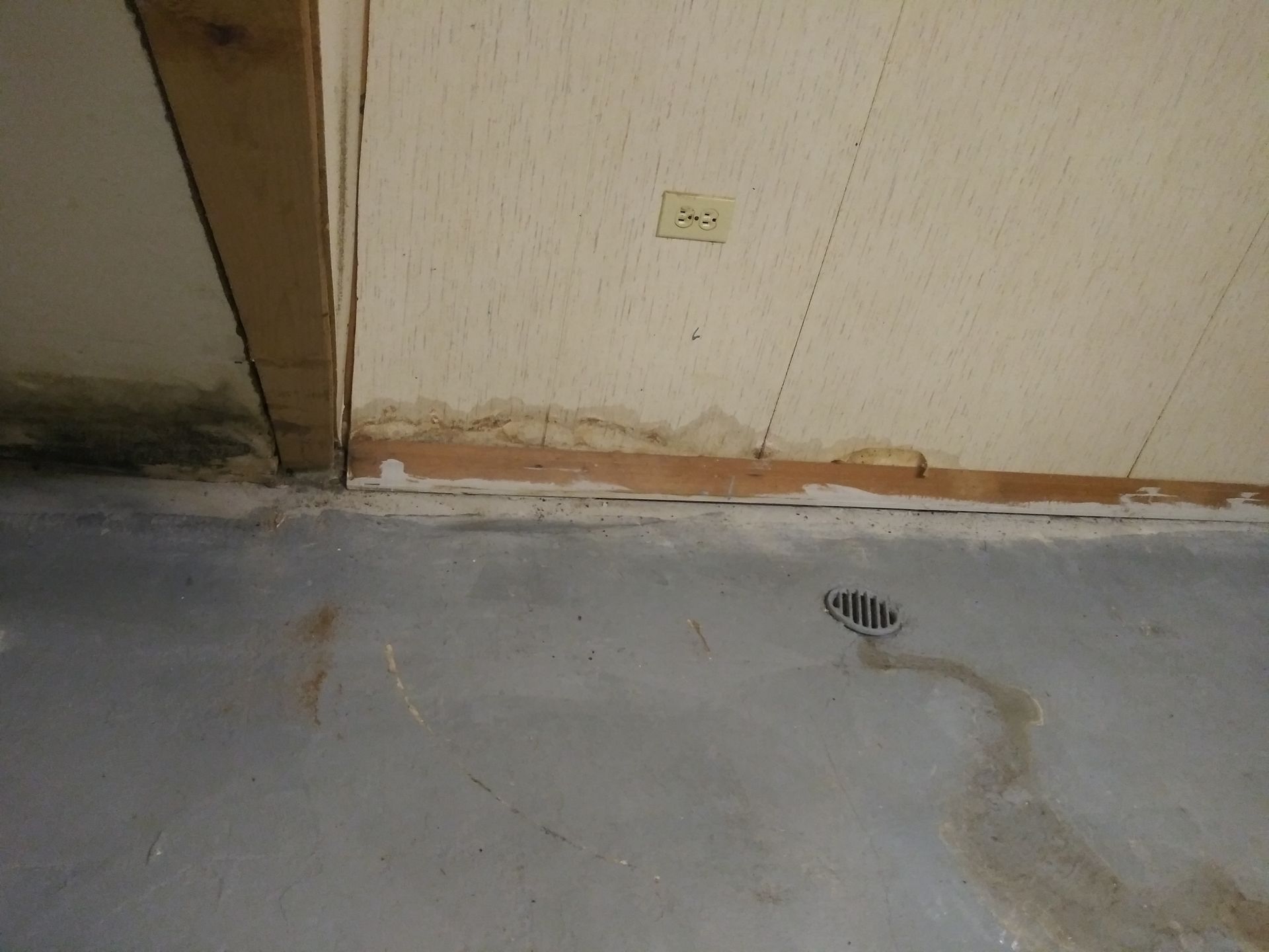 A drain on the floor of a room next to a wall.