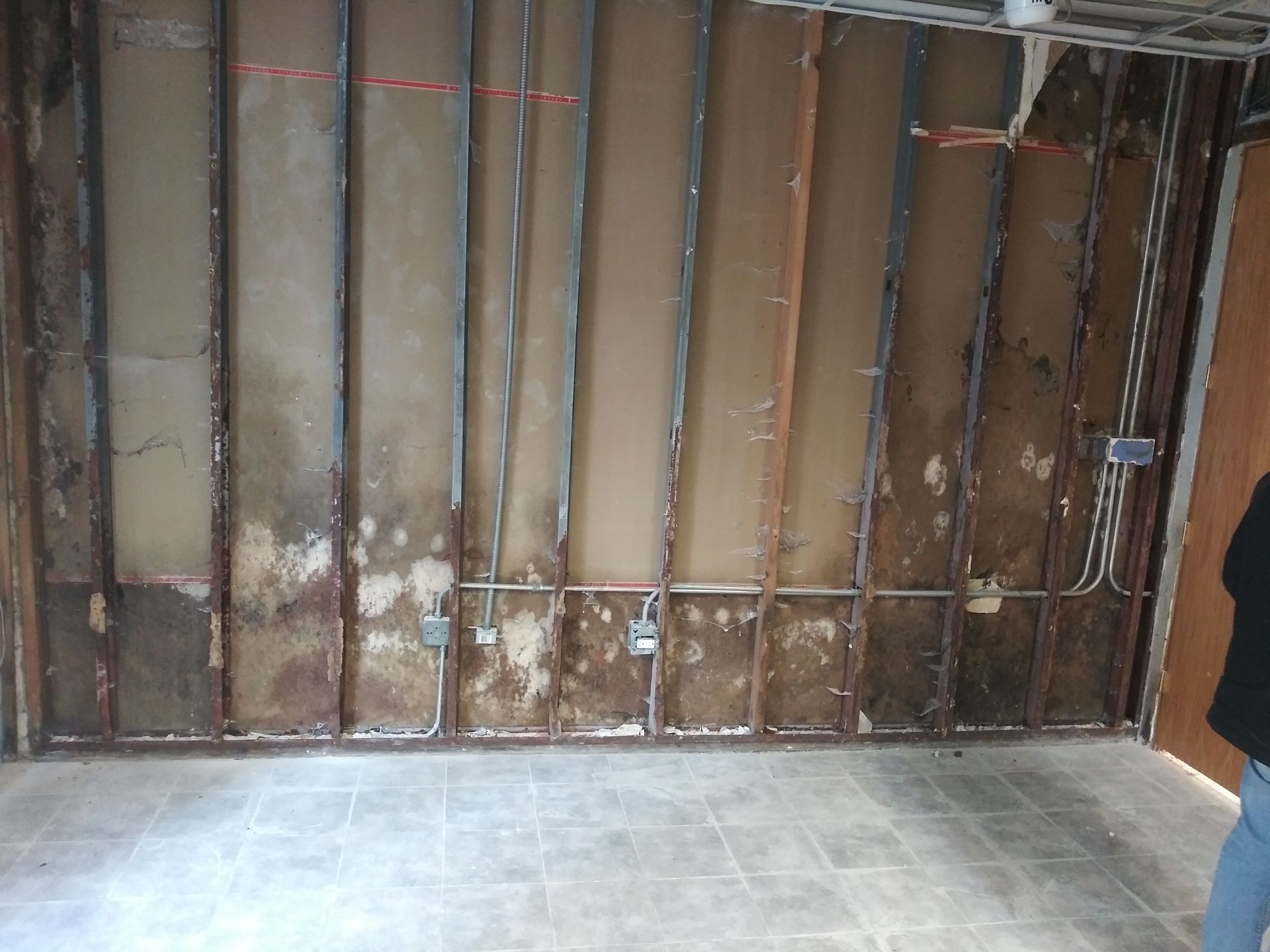 A person is standing in a room with a dirty wall and tile floor.