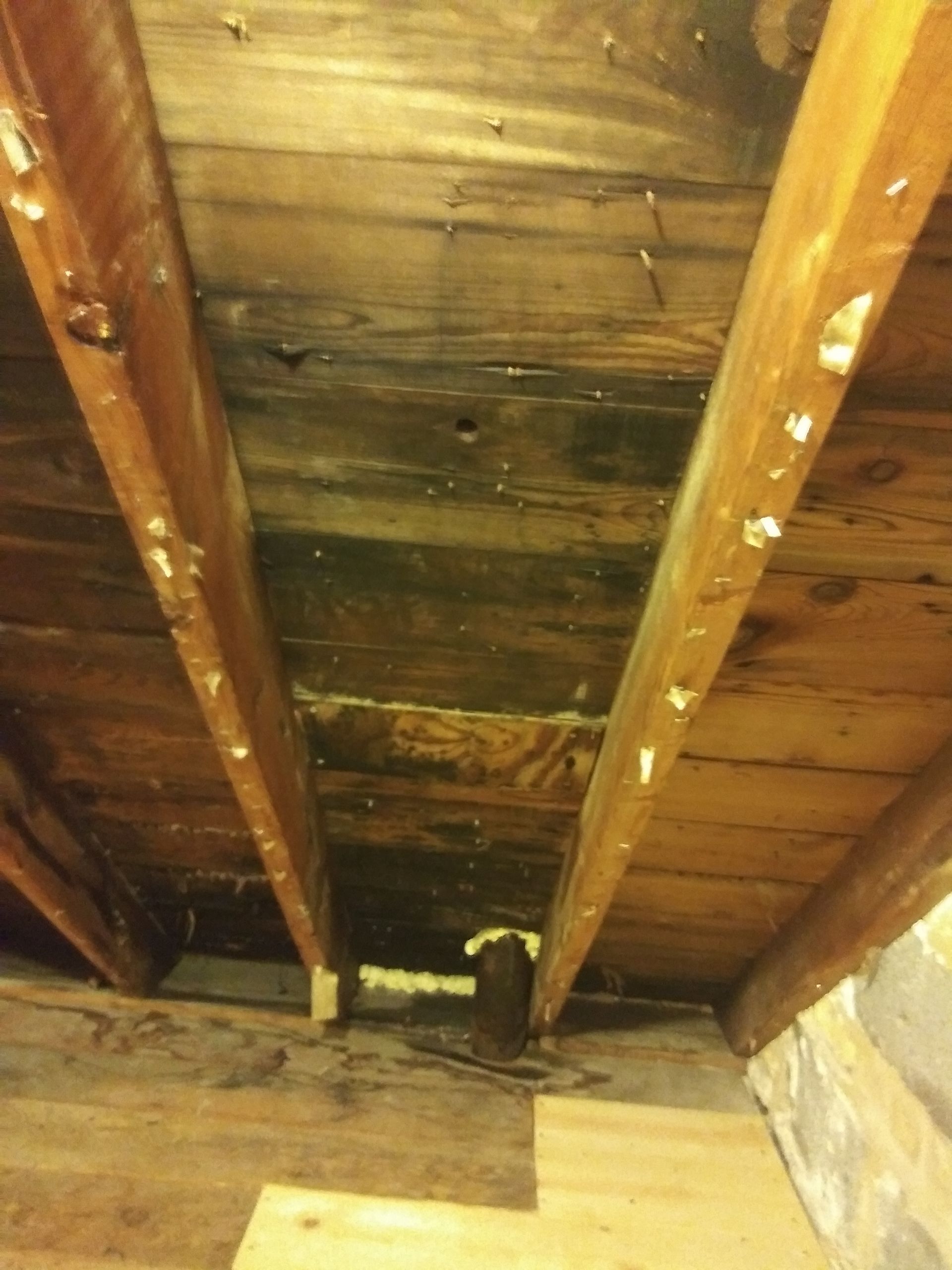 A wooden ceiling with a pipe in the middle of it.