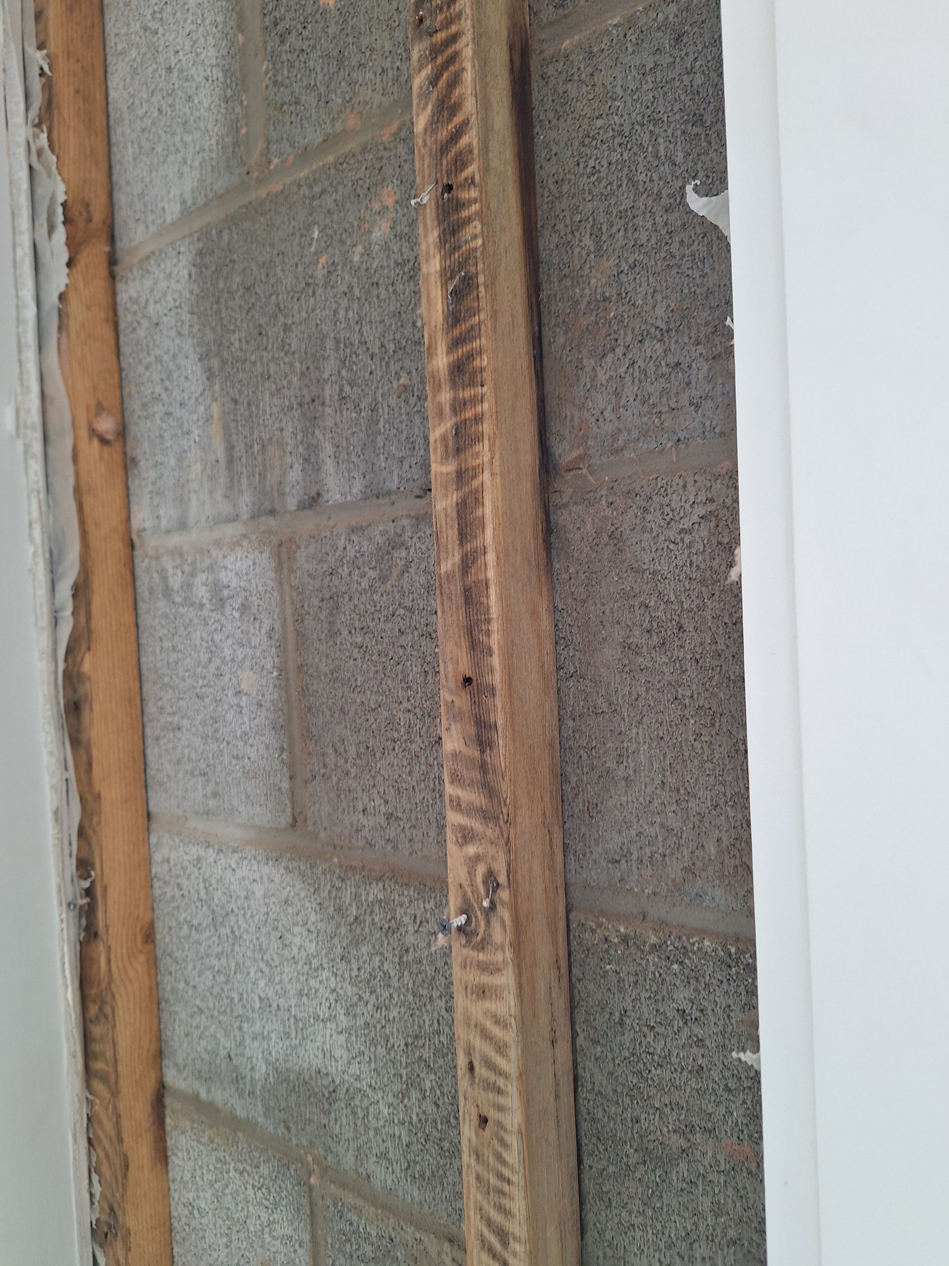 Gray cinder block wall with vertical wooden studs nailed in place, one at left and one at center.