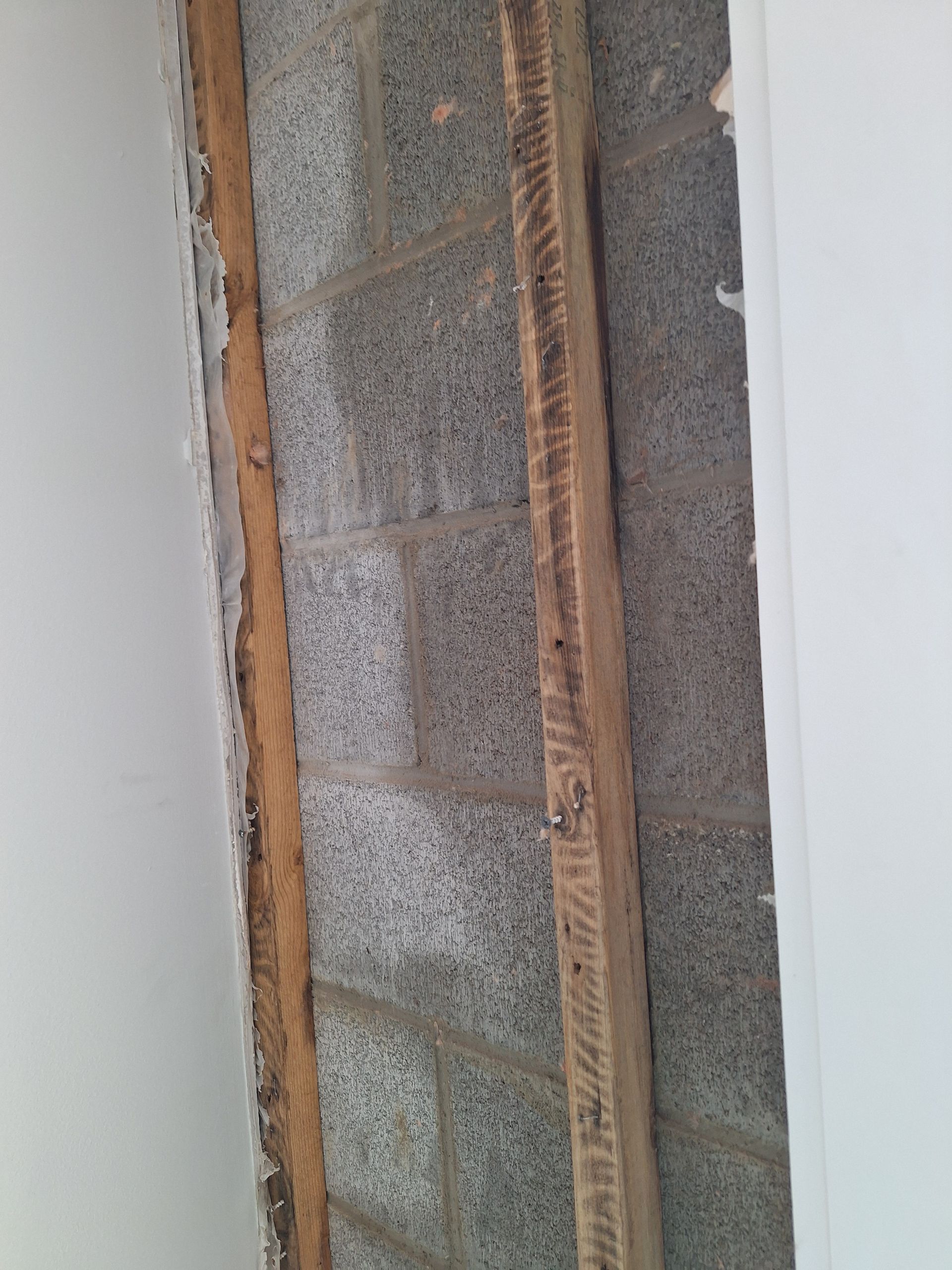 Exposed cinder block wall with wooden framing visible between interior wall surfaces.