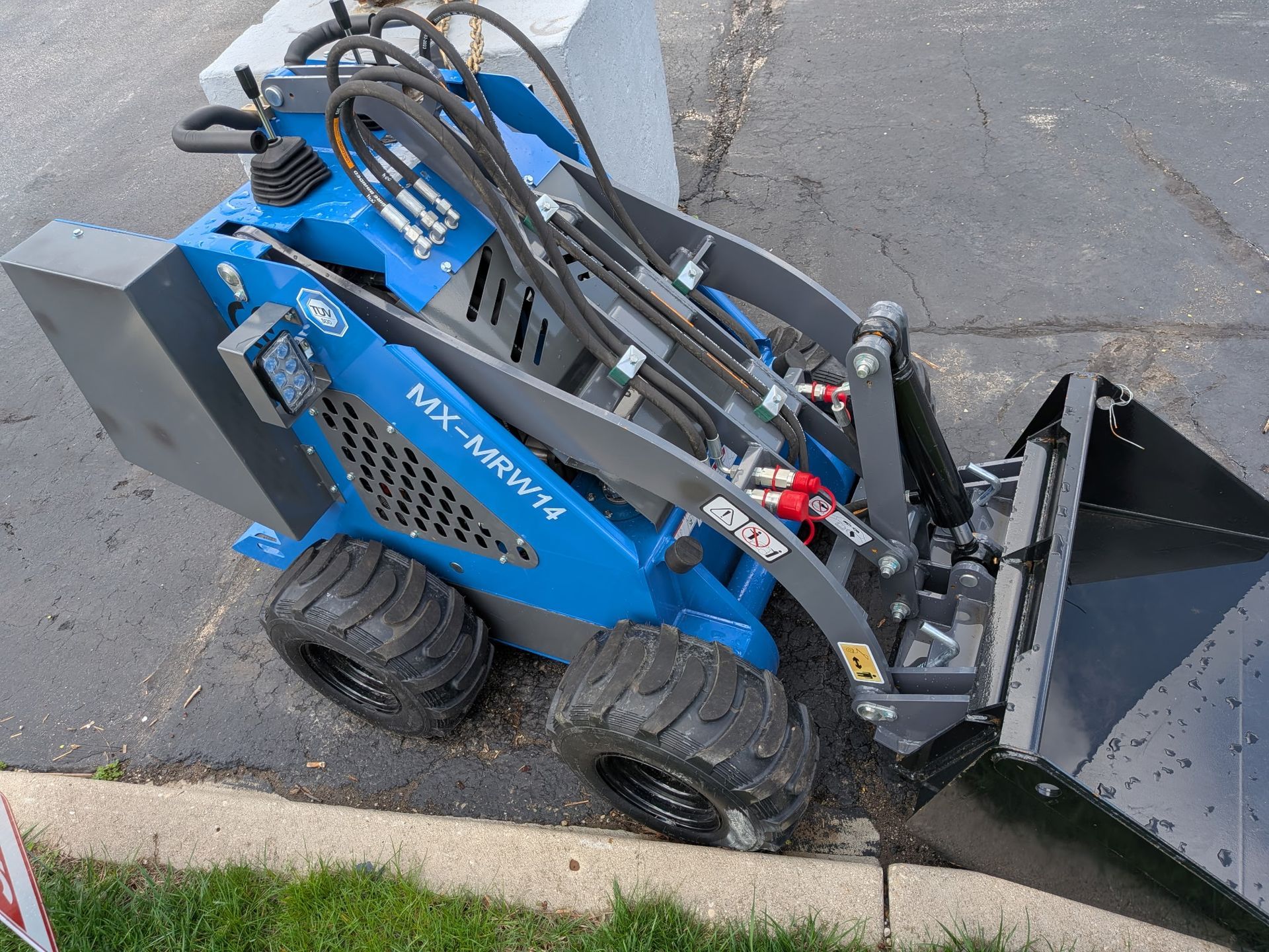 Blue skid steer with front bucket parked at curb on pavement