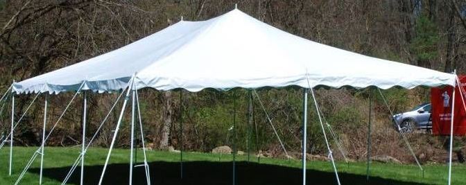 White canopy tent on a grassy field near trees and a red building.