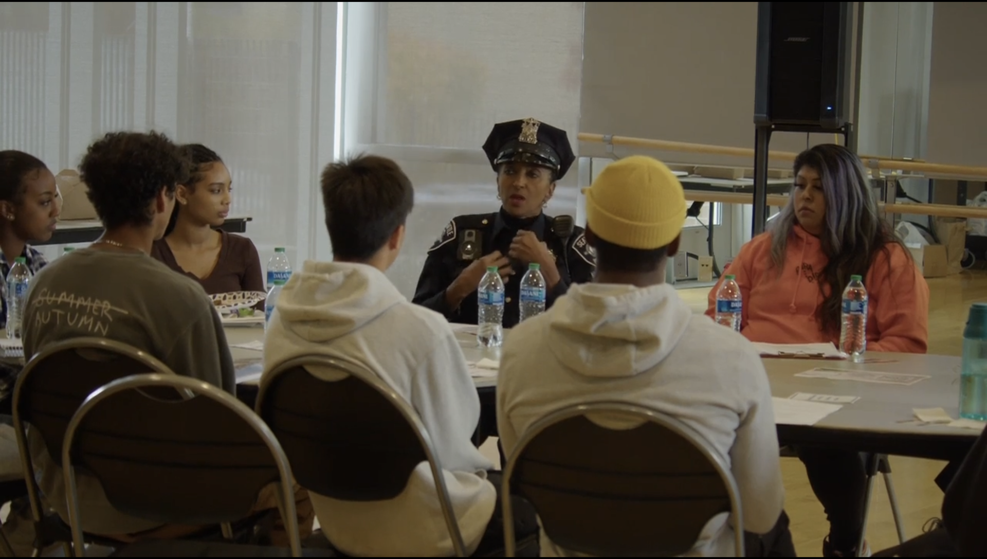 A group of people are sitting around a table with a police officer talking to them.