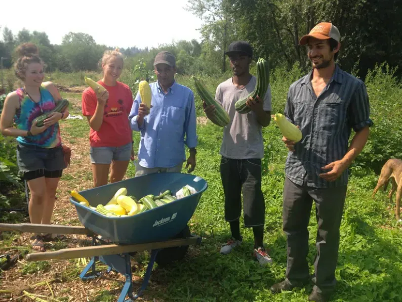 A group of people standing next to a wheelbarrow full of vegetables.