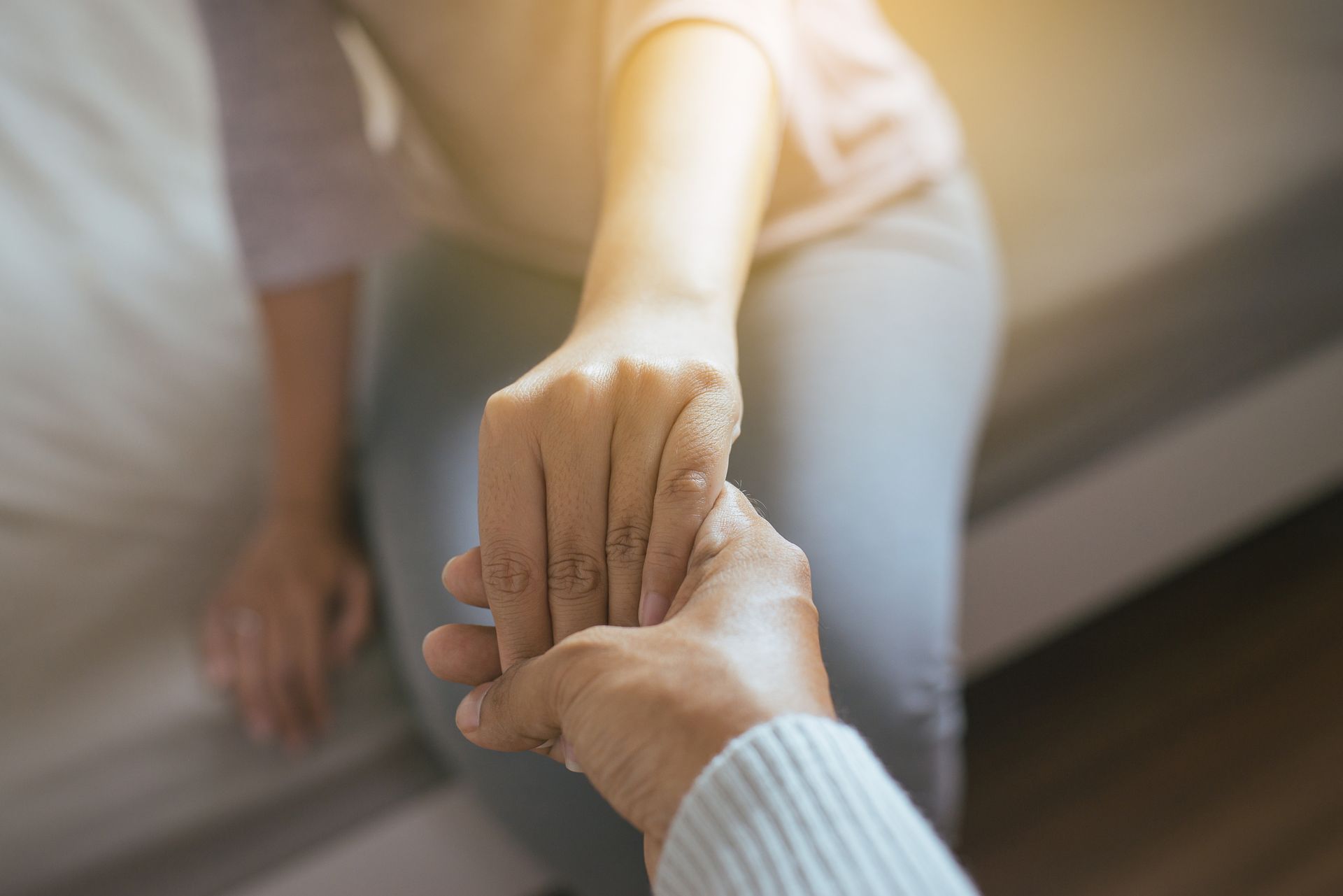 Two hands clasped, one reaching for support. Soft light, indoor setting.