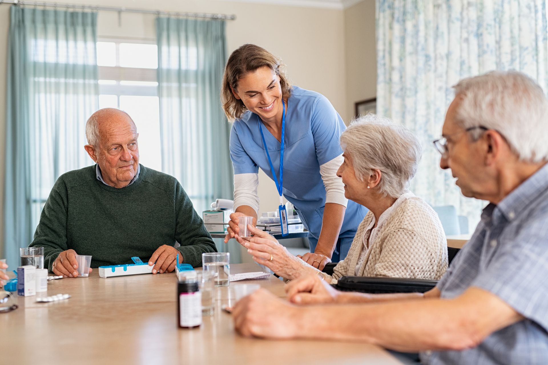Nurse giving medication to elderly people seated at a table.