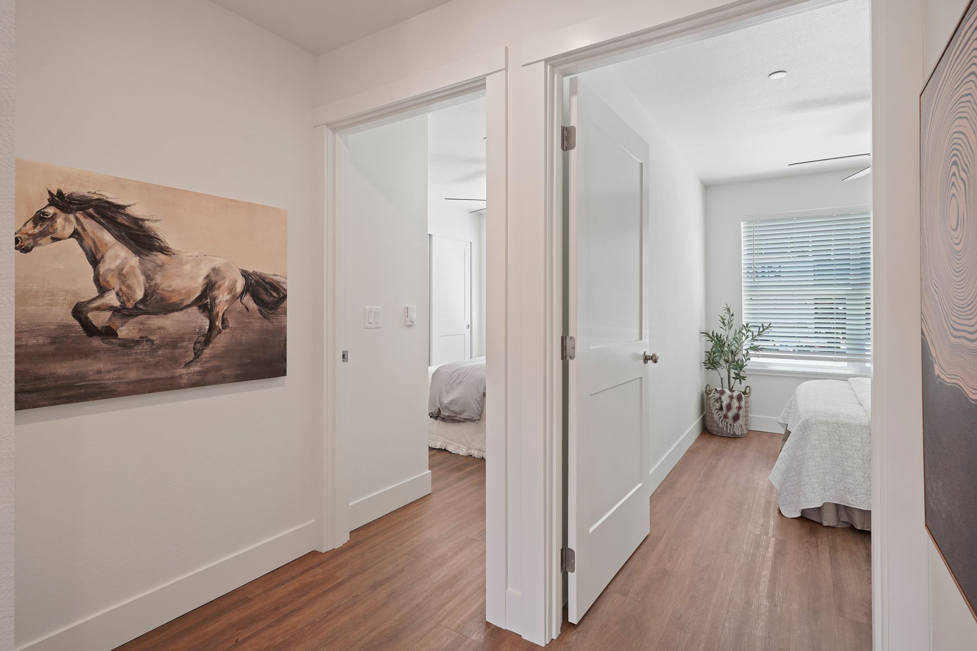 A hallway leading to a bedroom with a painting of a horse on the wall.