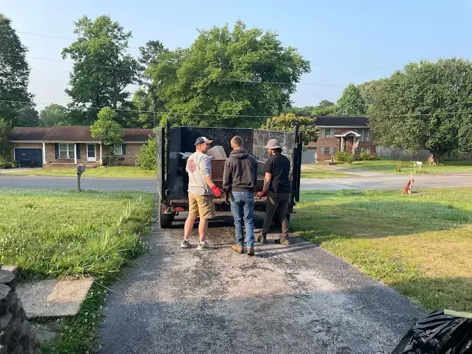 A group of people are standing in front of a dumpster.
