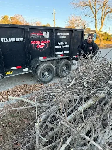 A man is standing next to a dumpster filled with branches.