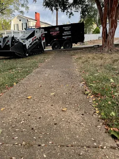 A bulldozer is parked on the side of a sidewalk next to a dumpster.
